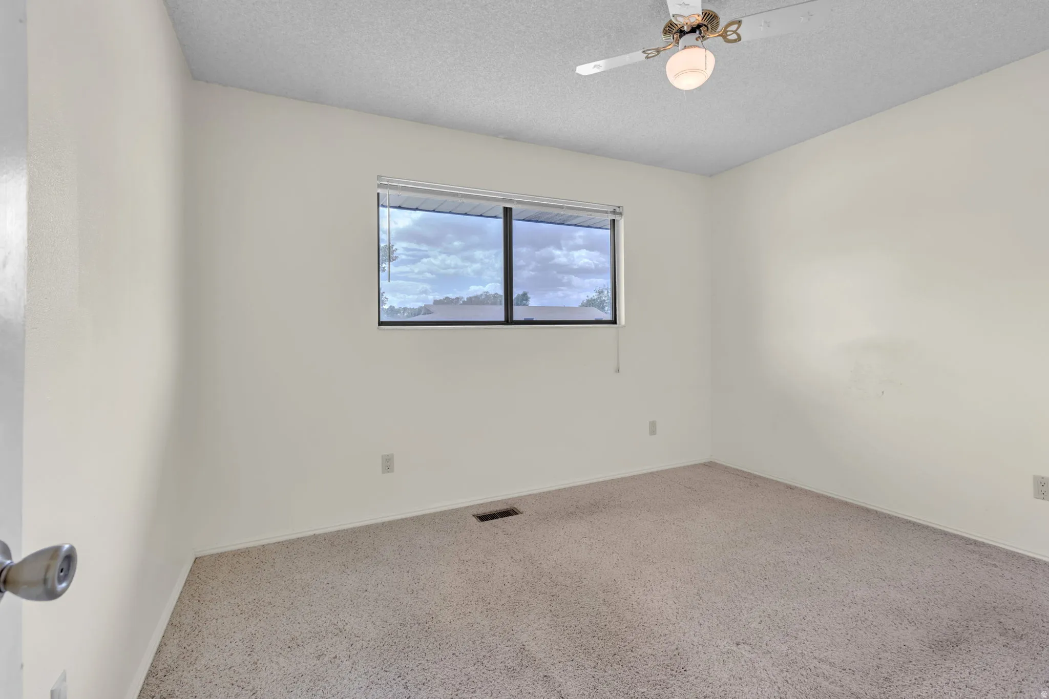 Carpeted room with a ceiling fan light fixture and a single window