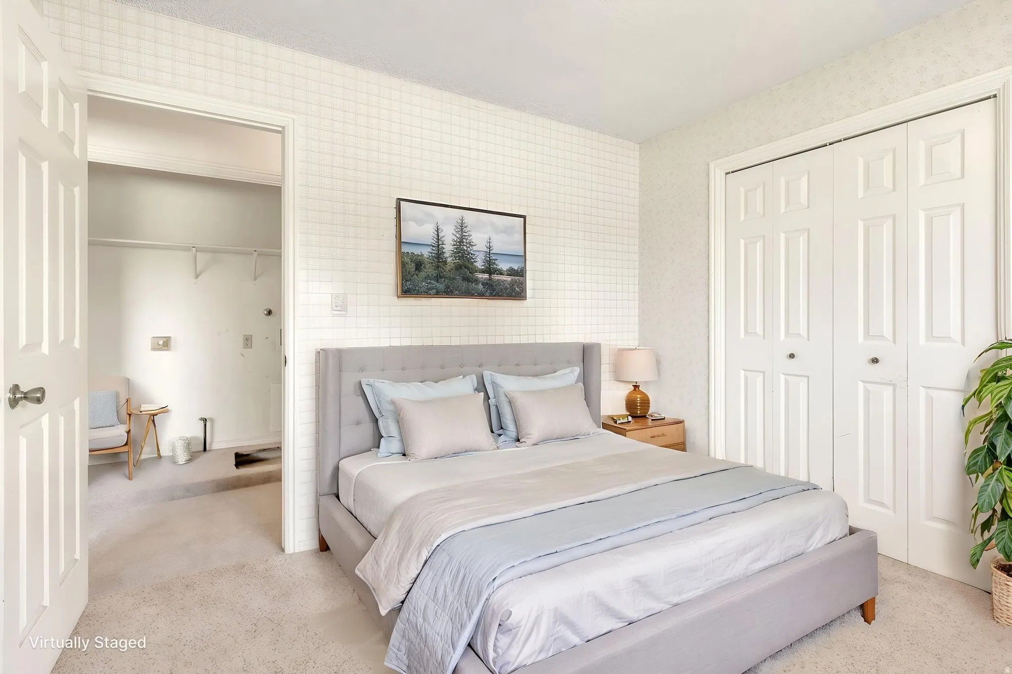 Virtually Staged -Carpeted bedroom with grid-patterned wallpaper, featuring two sets of bi-fold closet doors, a white paneled entry door, and an open doorway revealing a second closet space