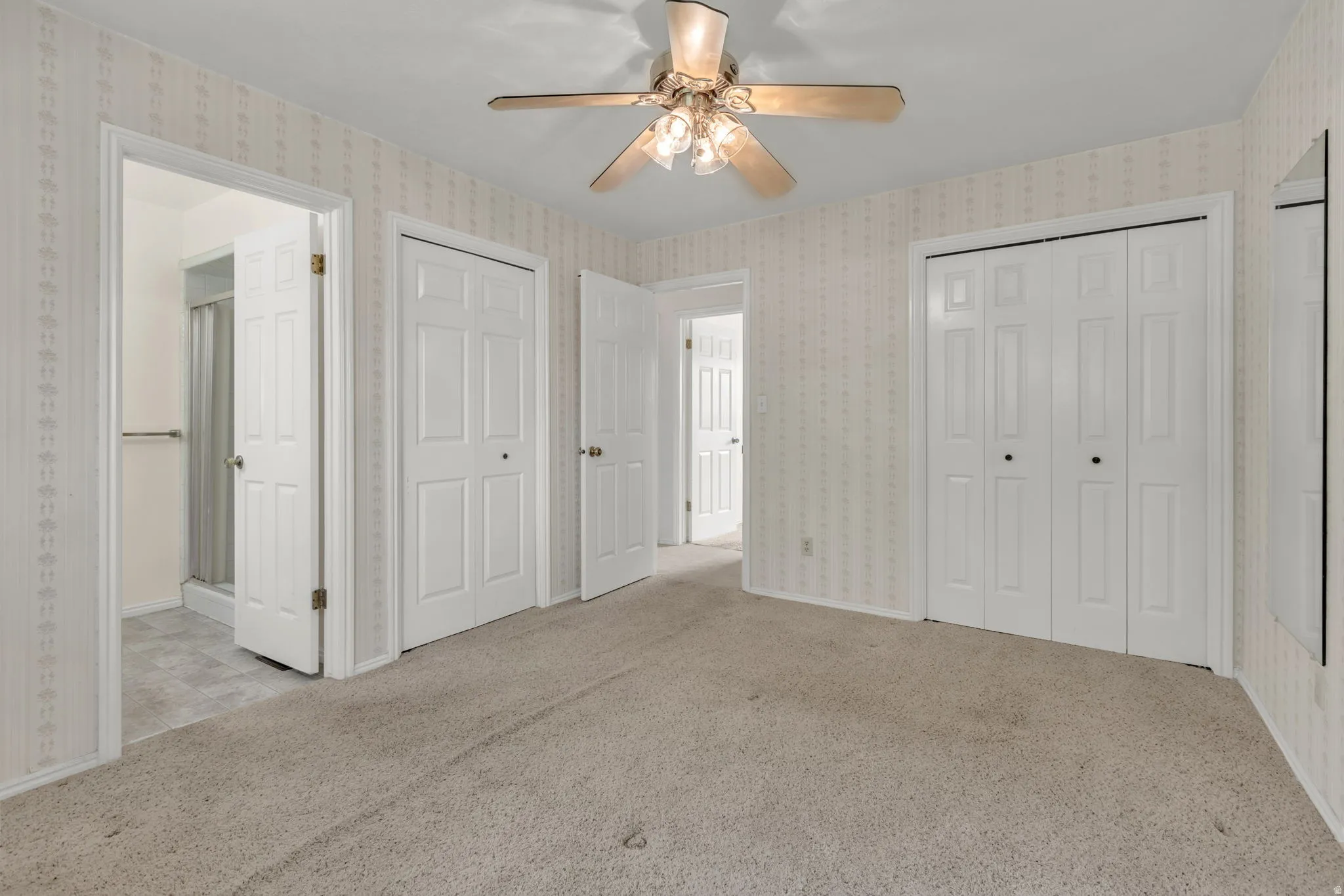Carpeted room featuring a ceiling fan with integrated lighting, multiple paneled doors, and direct access to a bathroom with a shower enclosure
