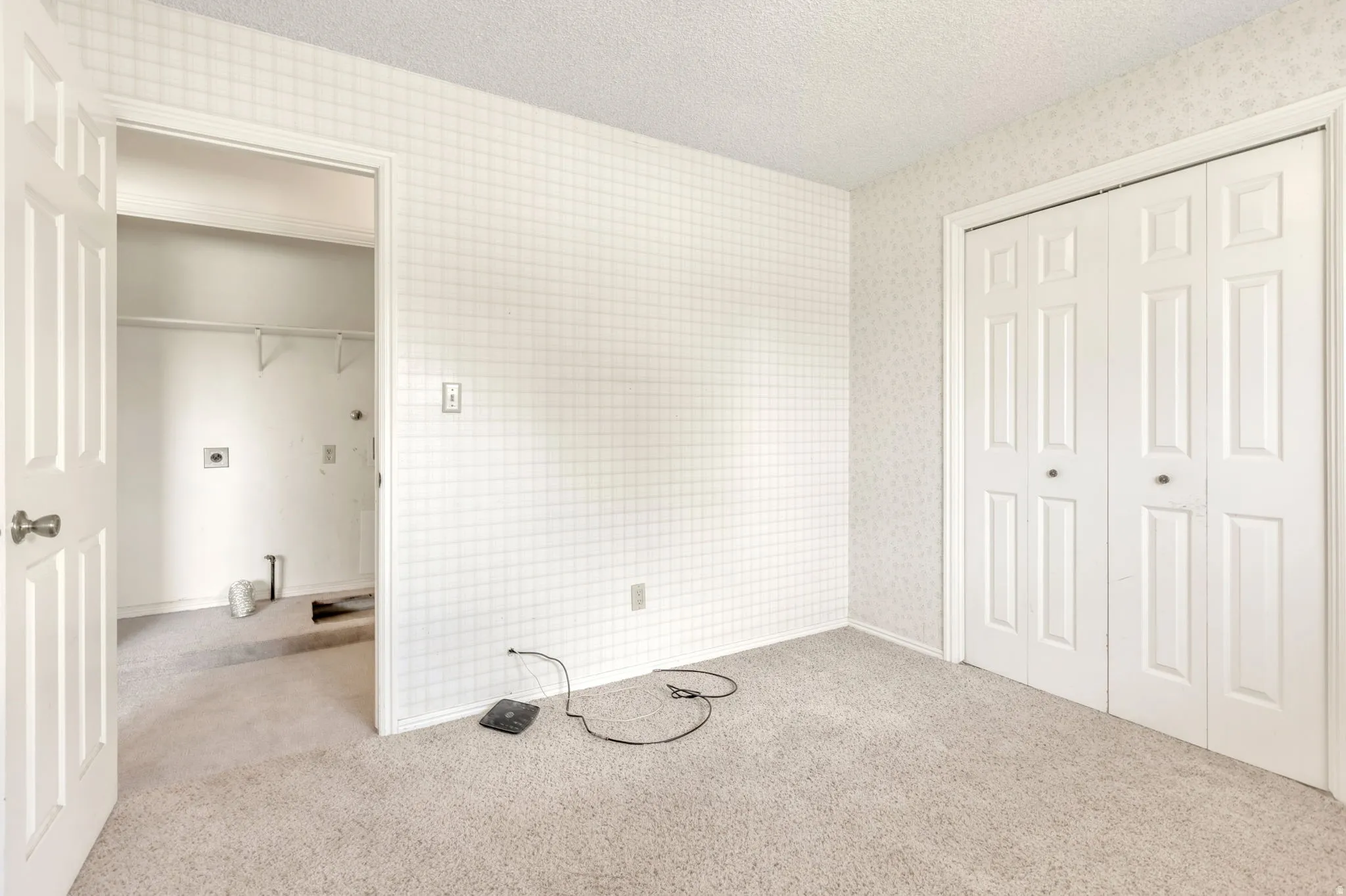 Carpeted room featuring a double-paneled bifold closet door and a white paneled door opening to a utility area with hookups and shelving