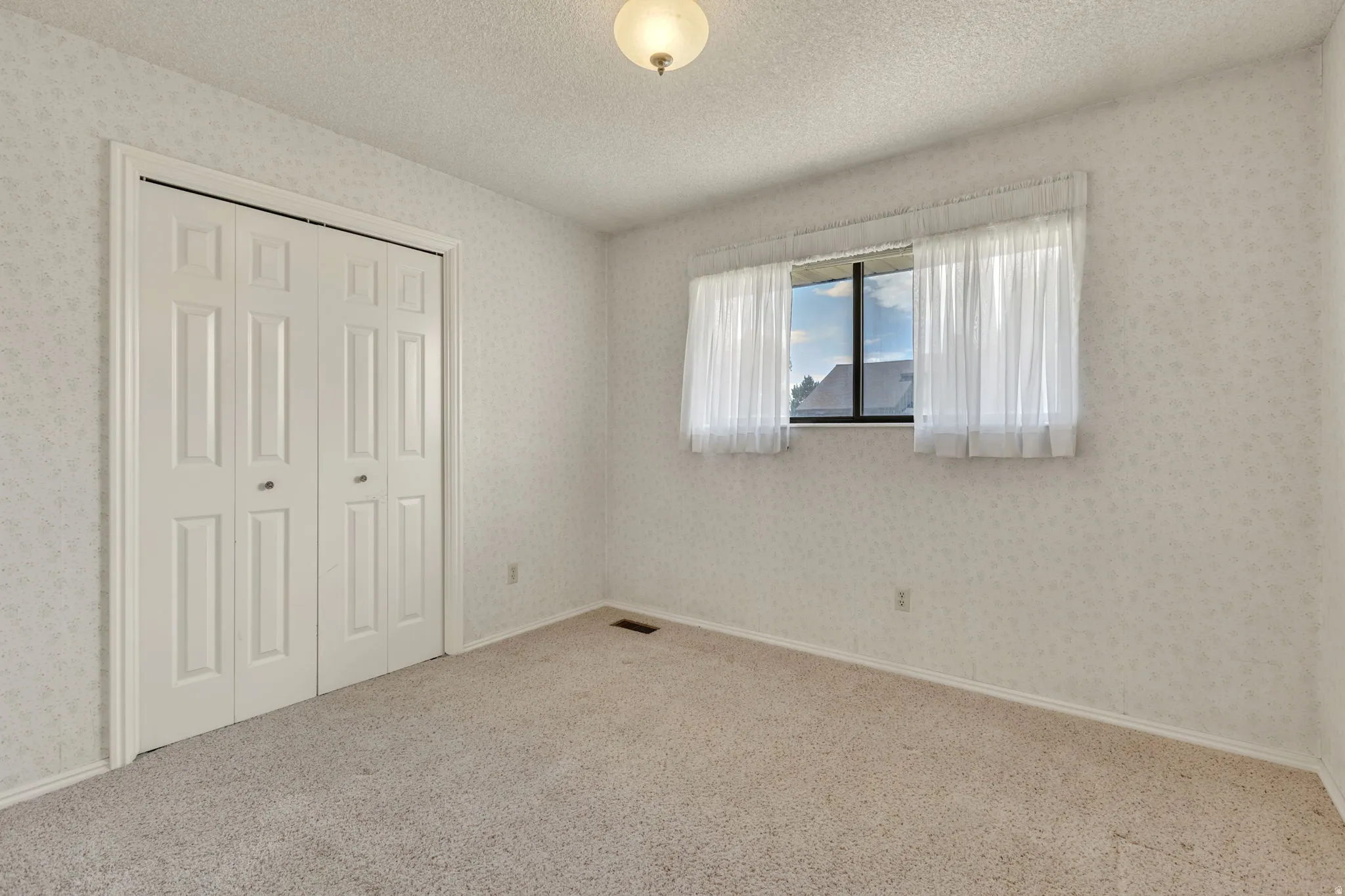Wall-to-wall carpeting and a ceiling-mounted light fixture define this room