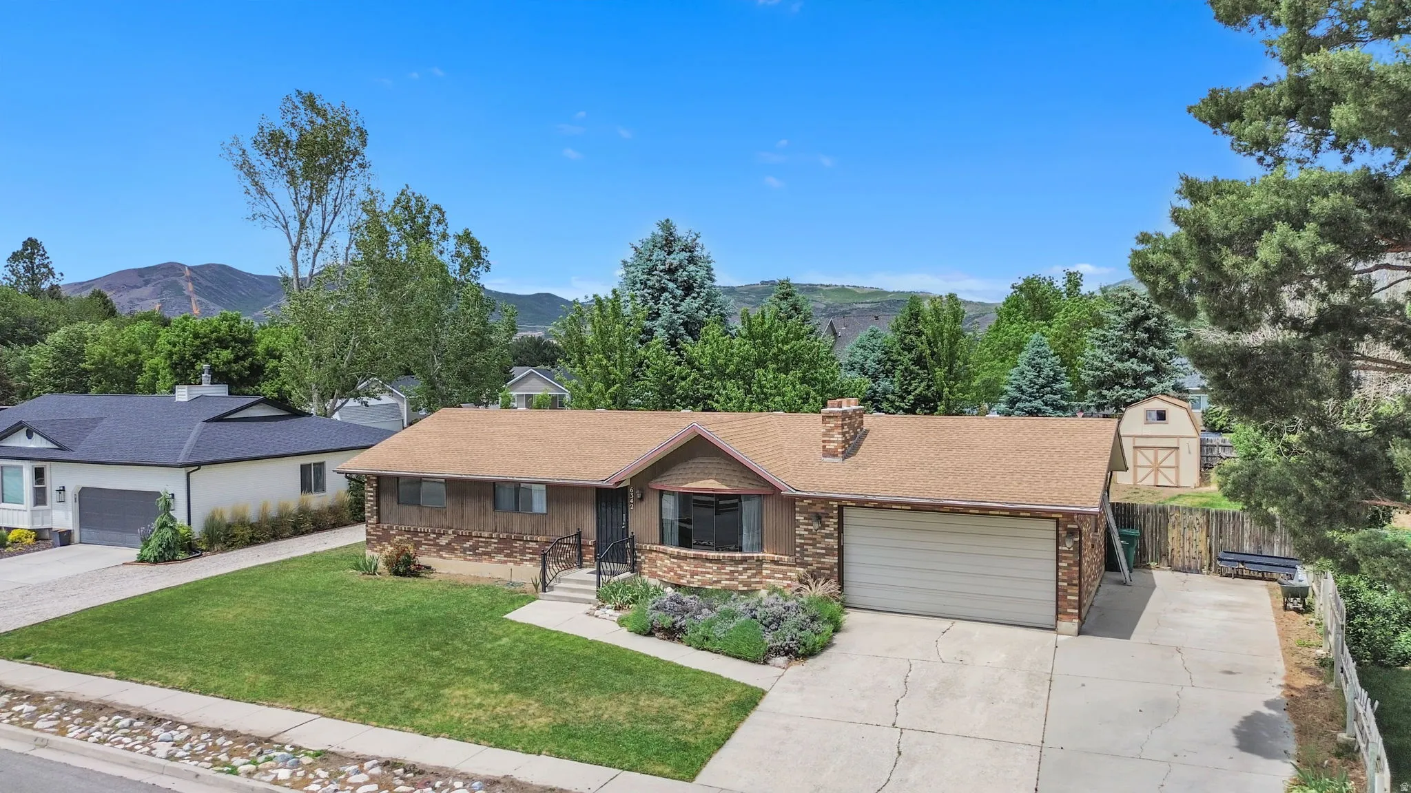 Ranch-style residence featuring a brick and wood-paneled exterior, attached garage, front yard with mature landscaping, and a backyard storage shed