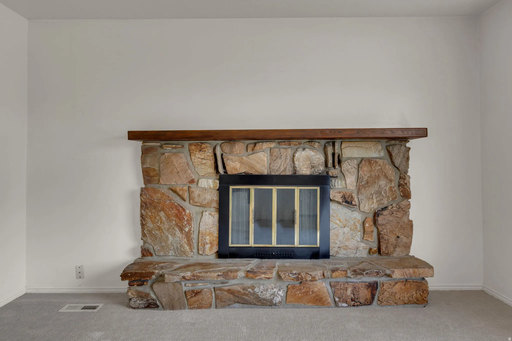 Stone fireplace featuring a wood mantel, a black firebox with glass doors, and a stone hearth
