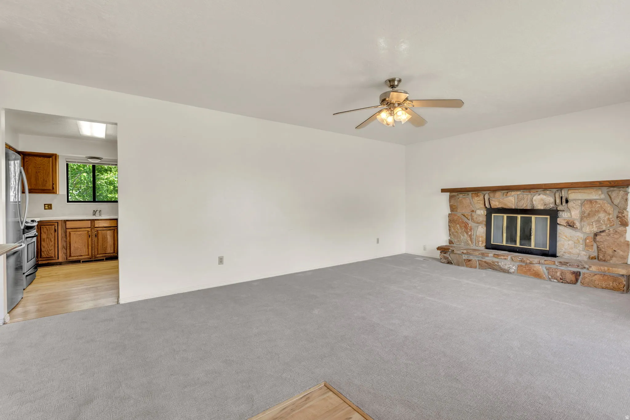 Spacious living area featuring a floor-to-ceiling stone fireplace, a ceiling fan, and light grey carpeting
