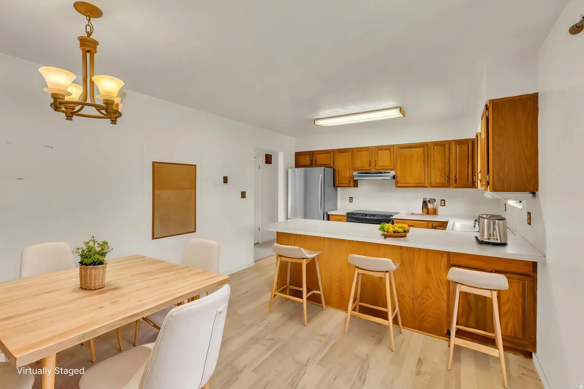 Virtually Staged -Open-concept kitchen and dining area featuring wood-finish flooring, a breakfast bar with countertop seating, wood cabinetry, and a full suite of stainless steel appliances