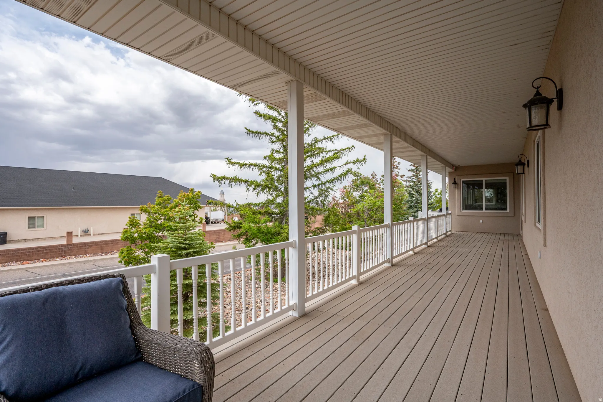 Expansive covered porch featuring composite decking, white railing, multiple recessed lights, and exterior wall sconces