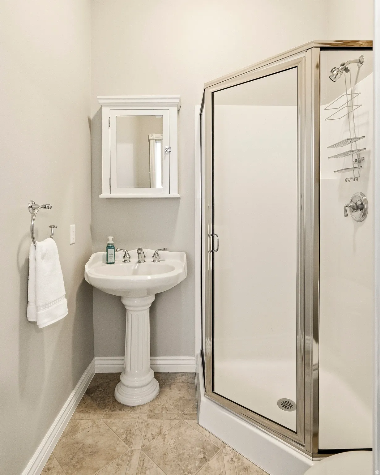 Pedestal sink with chrome fixtures, framed medicine cabinet, and a corner shower with a glass enclosure