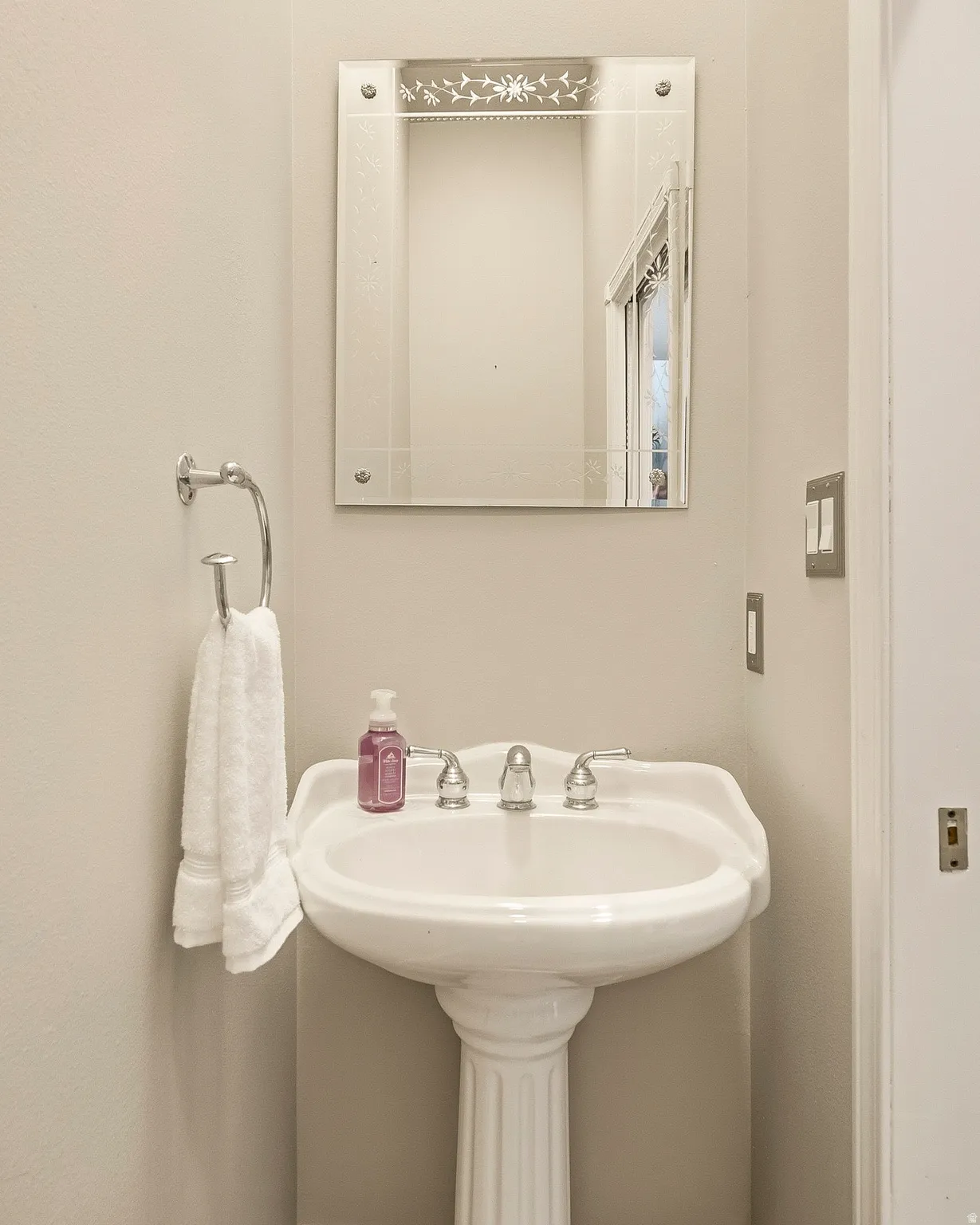 Pedestal sink with fluted base, polished chrome faucet, and an etched decorative mirror