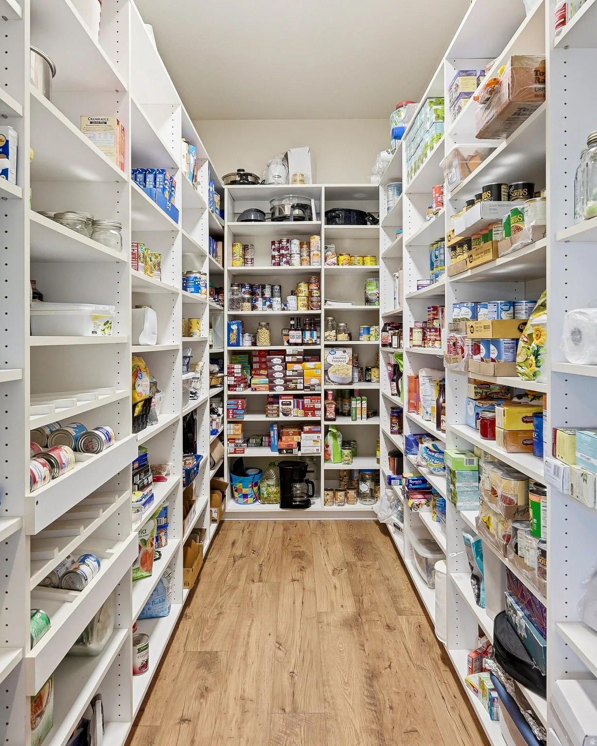 Spacious walk-in pantry featuring extensive white shelving, adjustable shelf heights, wood-finish flooring, and ample storage capacity