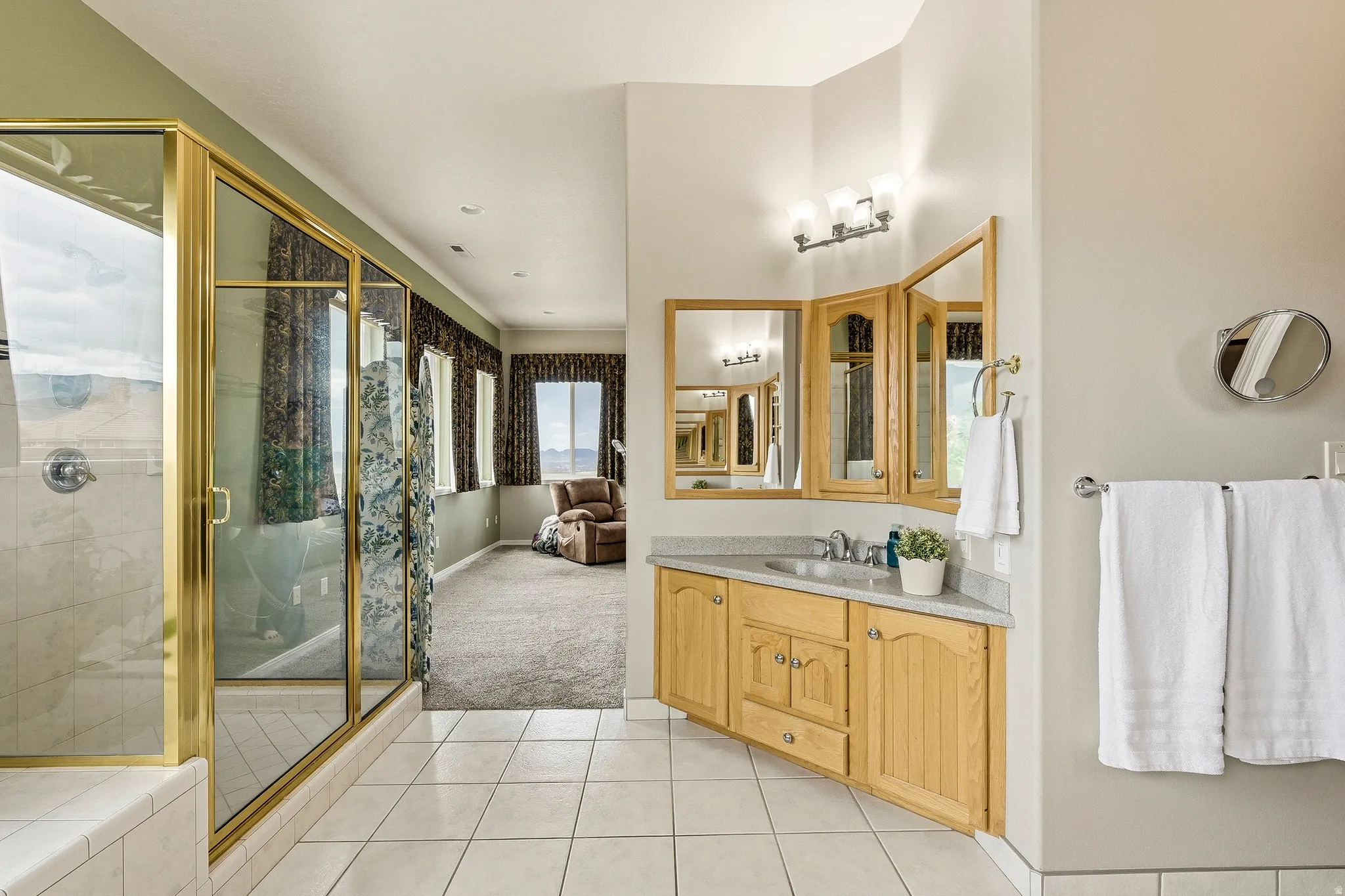Spacious bathroom featuring a corner vanity with light wood cabinetry, a built-in sink, and a multi-panel mirror