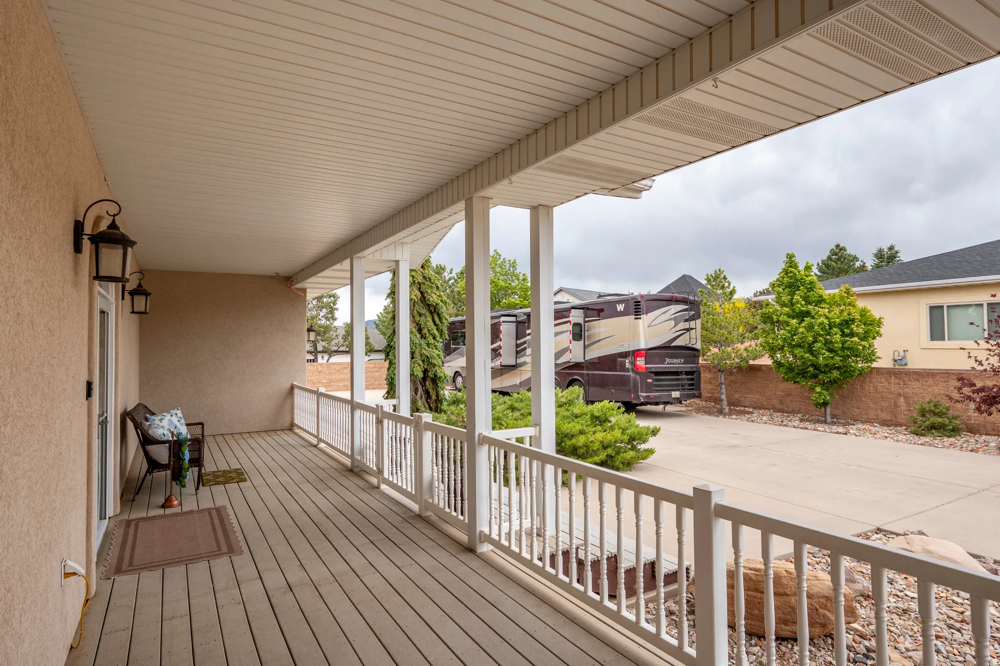 Expansive covered porch featuring wood-finish decking, white baluster railing, and two exterior sconces