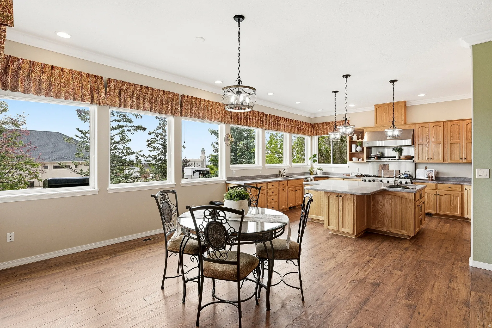 Open-concept kitchen and dining area featuring wood-finish flooring, extensive window line, light wood cabinetry, a central island with countertop seating, and recessed lighting