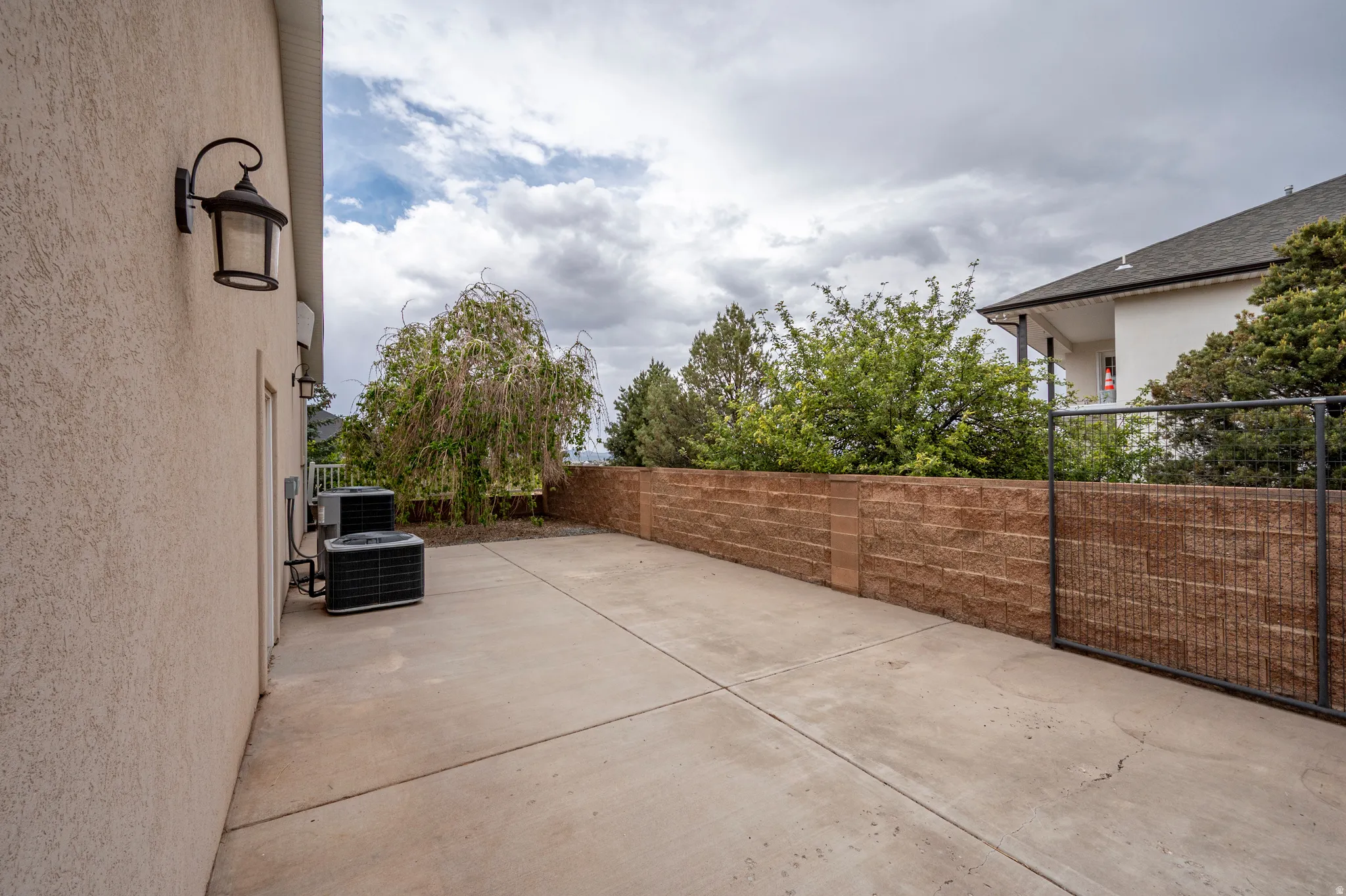Concrete patio area featuring a textured stucco exterior, a decorative wall-mounted light fixture, and two outdoor HVAC units