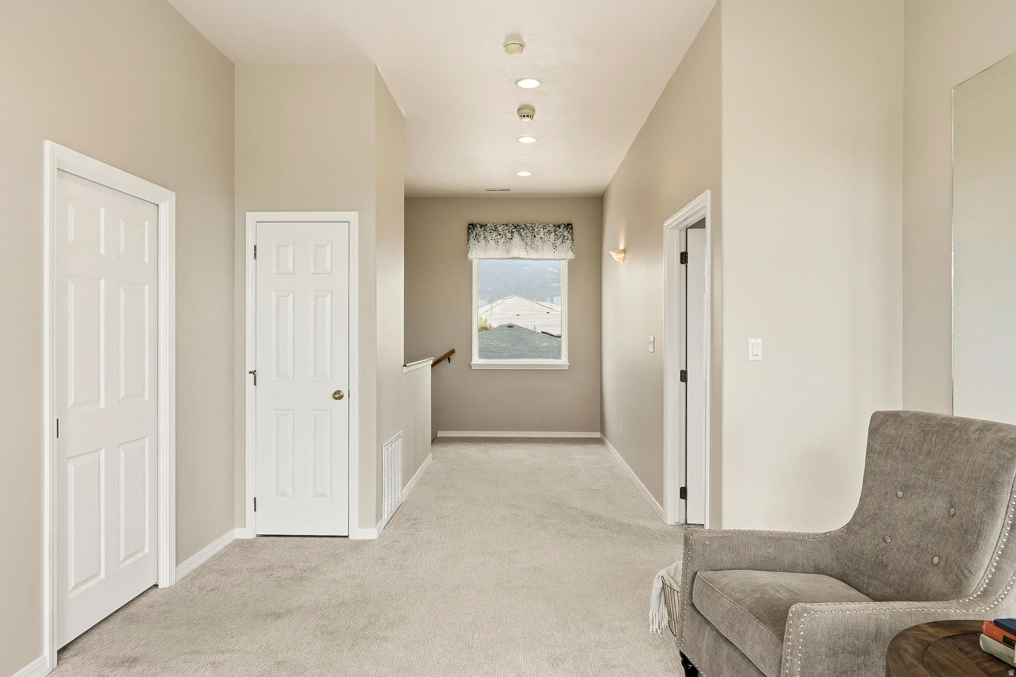 Carpeted hallway featuring a window with valance, recessed lighting, and wall sconces