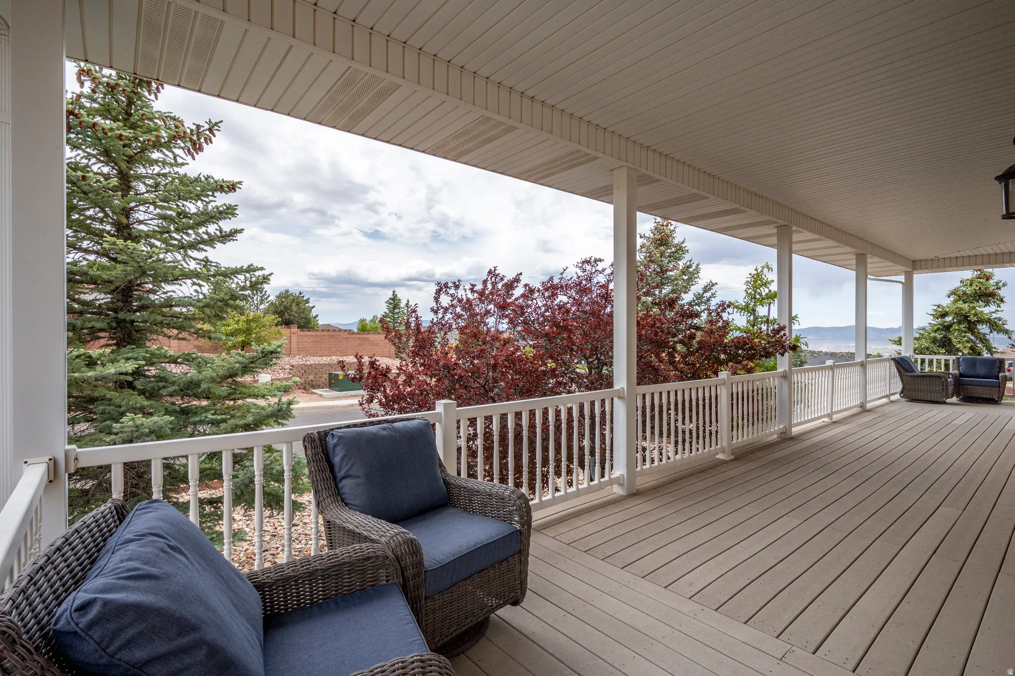 Expansive covered porch featuring a painted wood-finish deck, white railing, and decorative ceiling panels