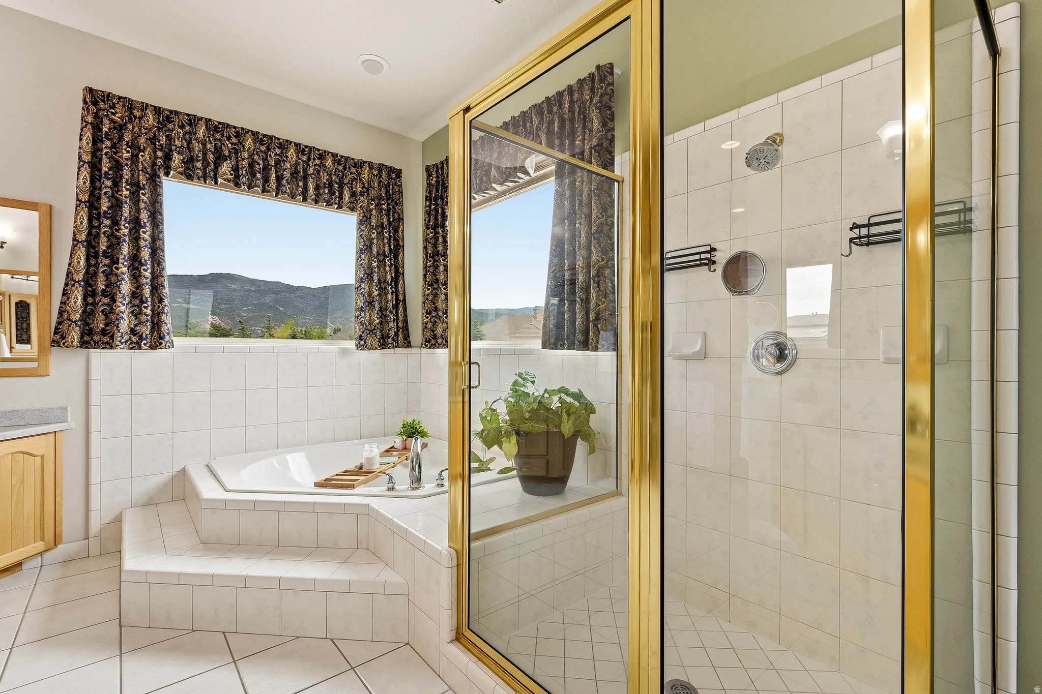 Bathroom featuring a built-in corner soaking tub with tiled surround, a separate glass-enclosed shower with gold-toned framing, and a large horizontal window