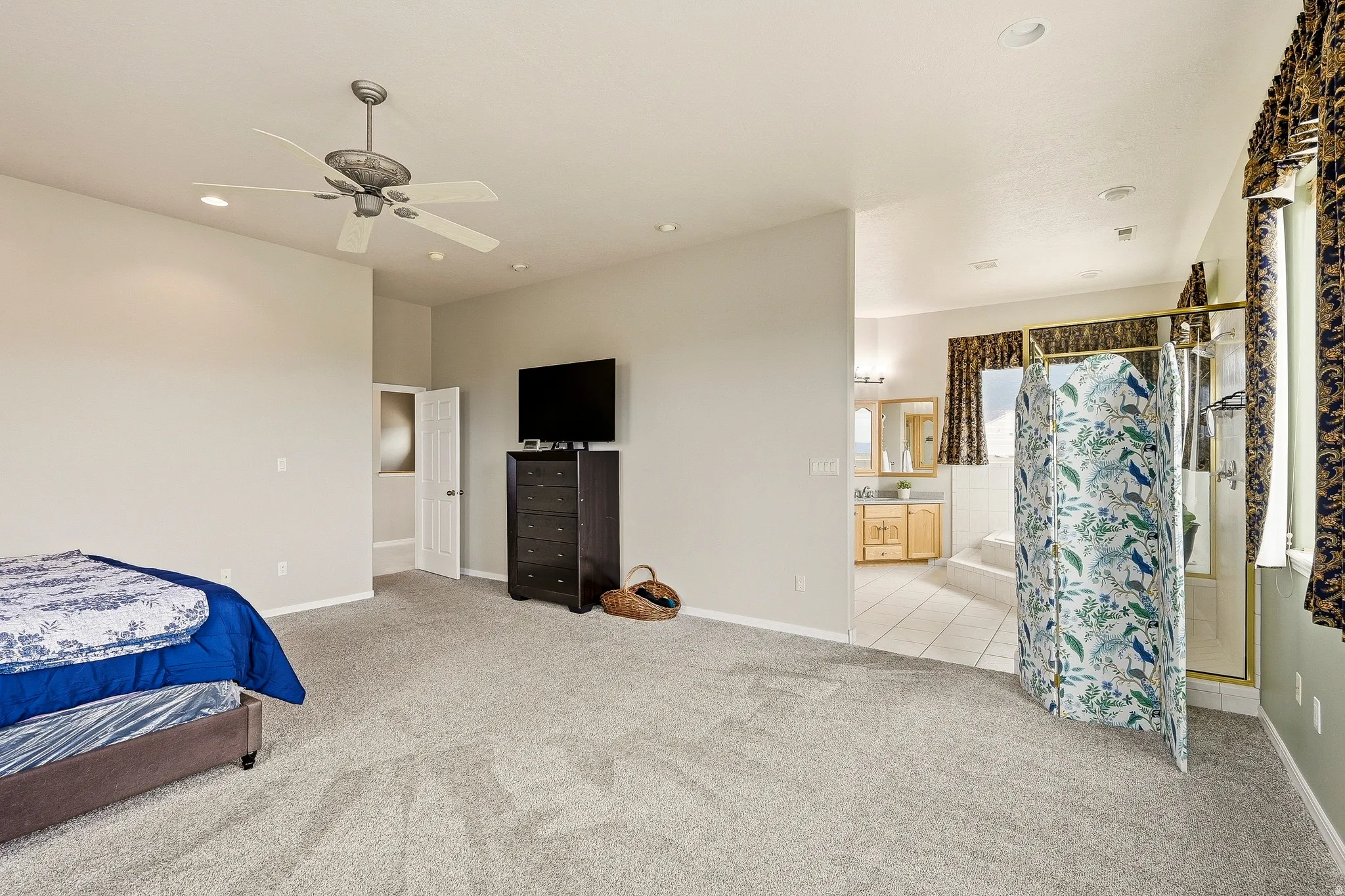 Spacious carpeted room featuring a ceiling fan with integrated lighting, recessed lighting, and a doorway to a tiled area with a built-in tub and vanity
