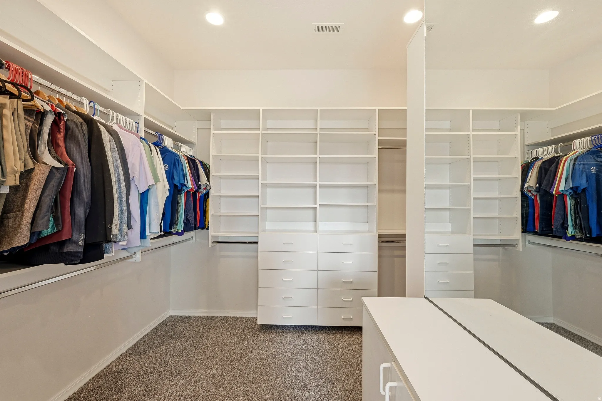 Custom closet system featuring extensive built-in shelving, multiple hanging rods, integrated drawer units, recessed lighting, and a central island with a solid surface top