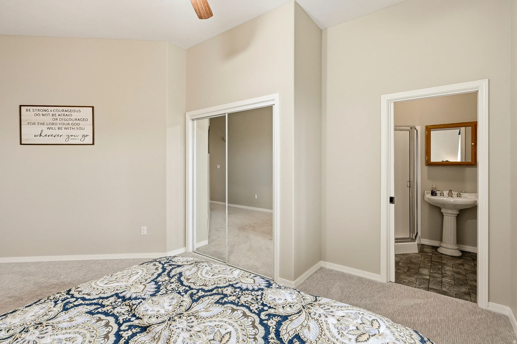 Bedroom featuring plush carpeting, a mirrored sliding closet door, and a ceiling fan