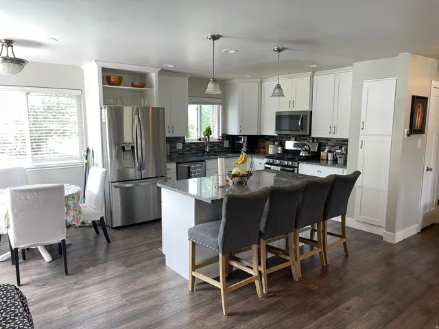 Modern kitchen featuring a granite-topped island with seating, stainless steel appliances, white cabinetry, and wood-finish flooring