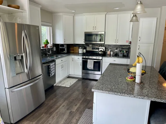 Kitchen featuring white shaker cabinetry, stainless steel appliances, dark wood-finish flooring, and a central island with a granite countertop