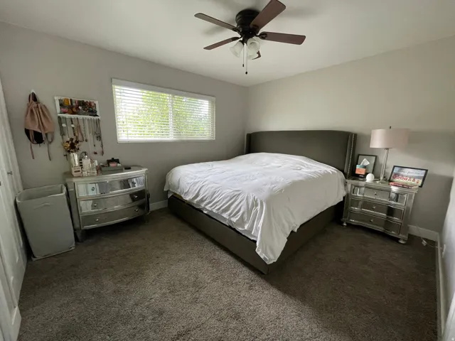 Carpeted room featuring a ceiling fan with light fixture, a window with horizontal blinds, and neutral wall tones