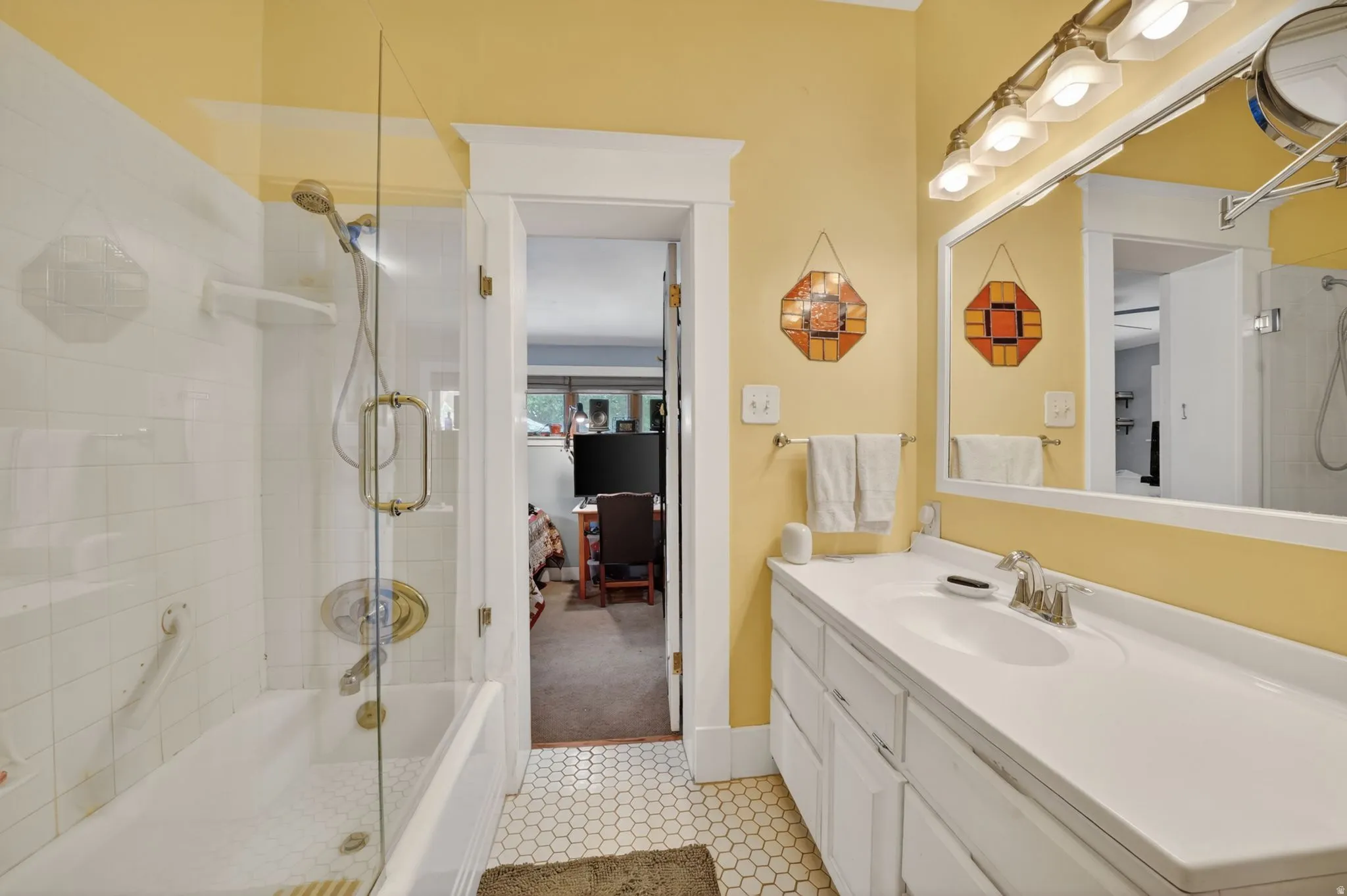 Bathroom featuring a glass-enclosed shower-over-tub combination with white subway tile surround, a single vanity with an integrated sink and white countertop, and hexagonal floor tiling