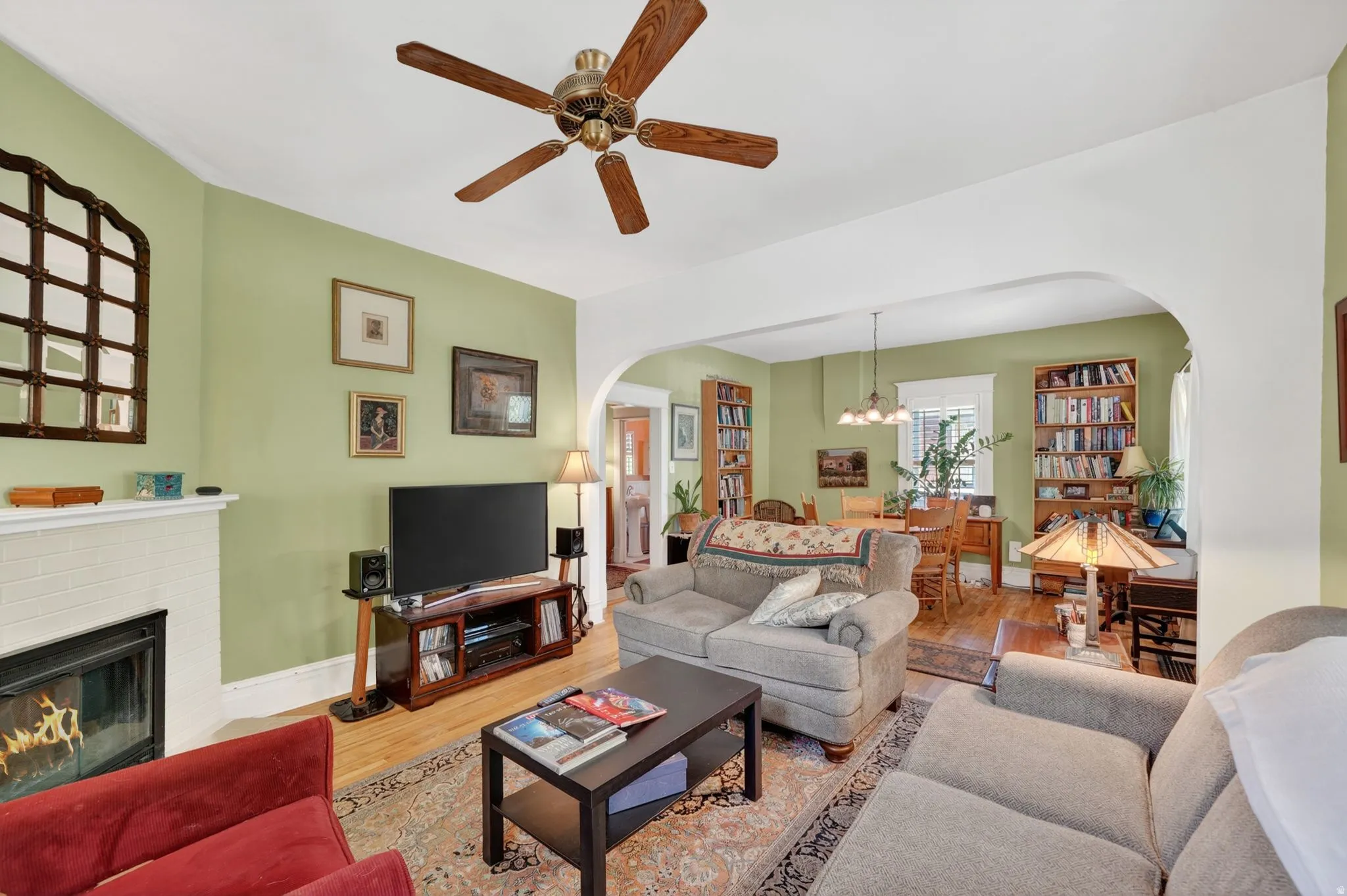 Living area featuring hardwood flooring, a ceiling fan, and a fireplace with a white tile surround