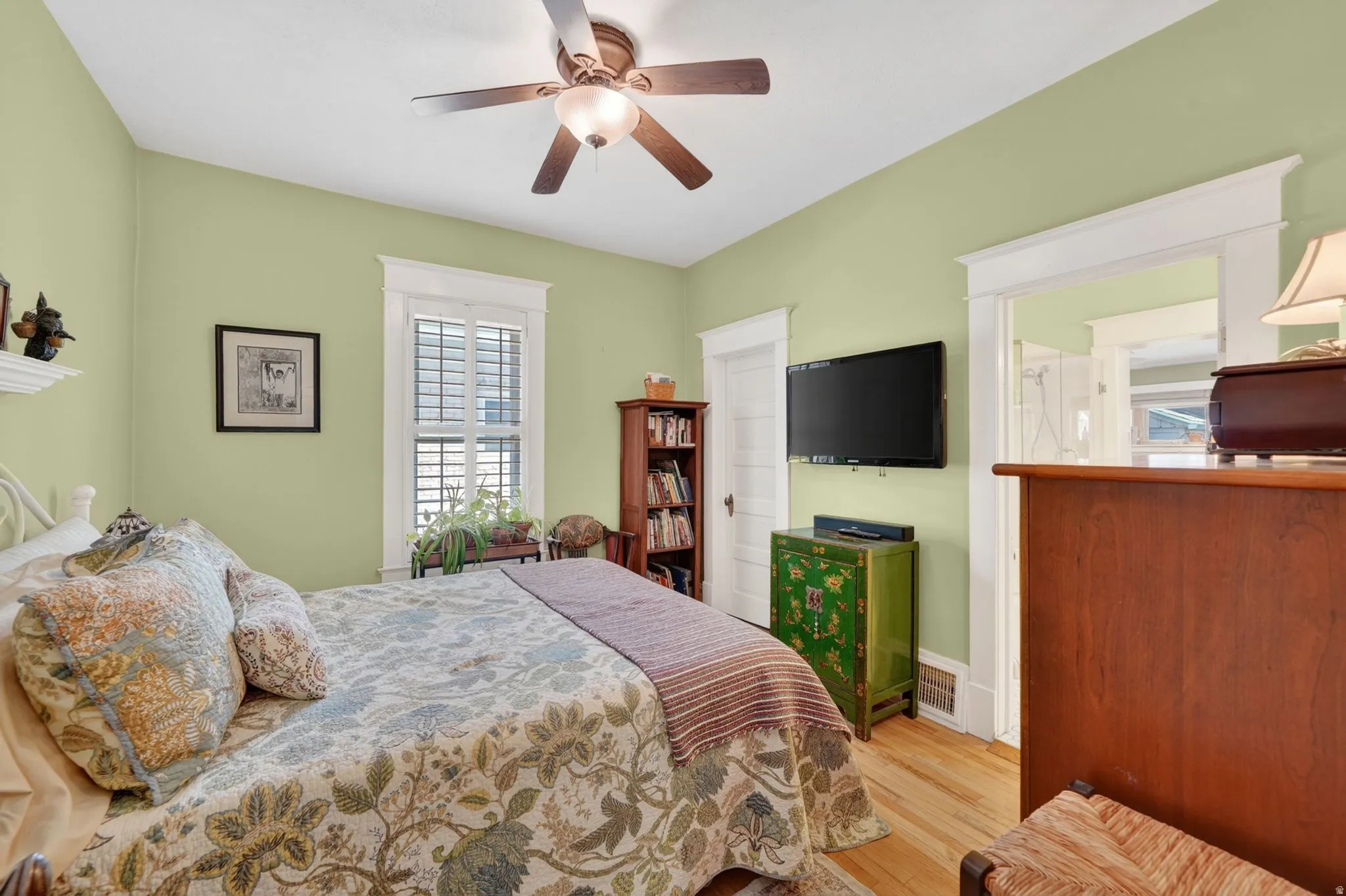Brightly painted interior featuring a ceiling fan, wood-finish flooring, white trim details, and a window with plantation shutters