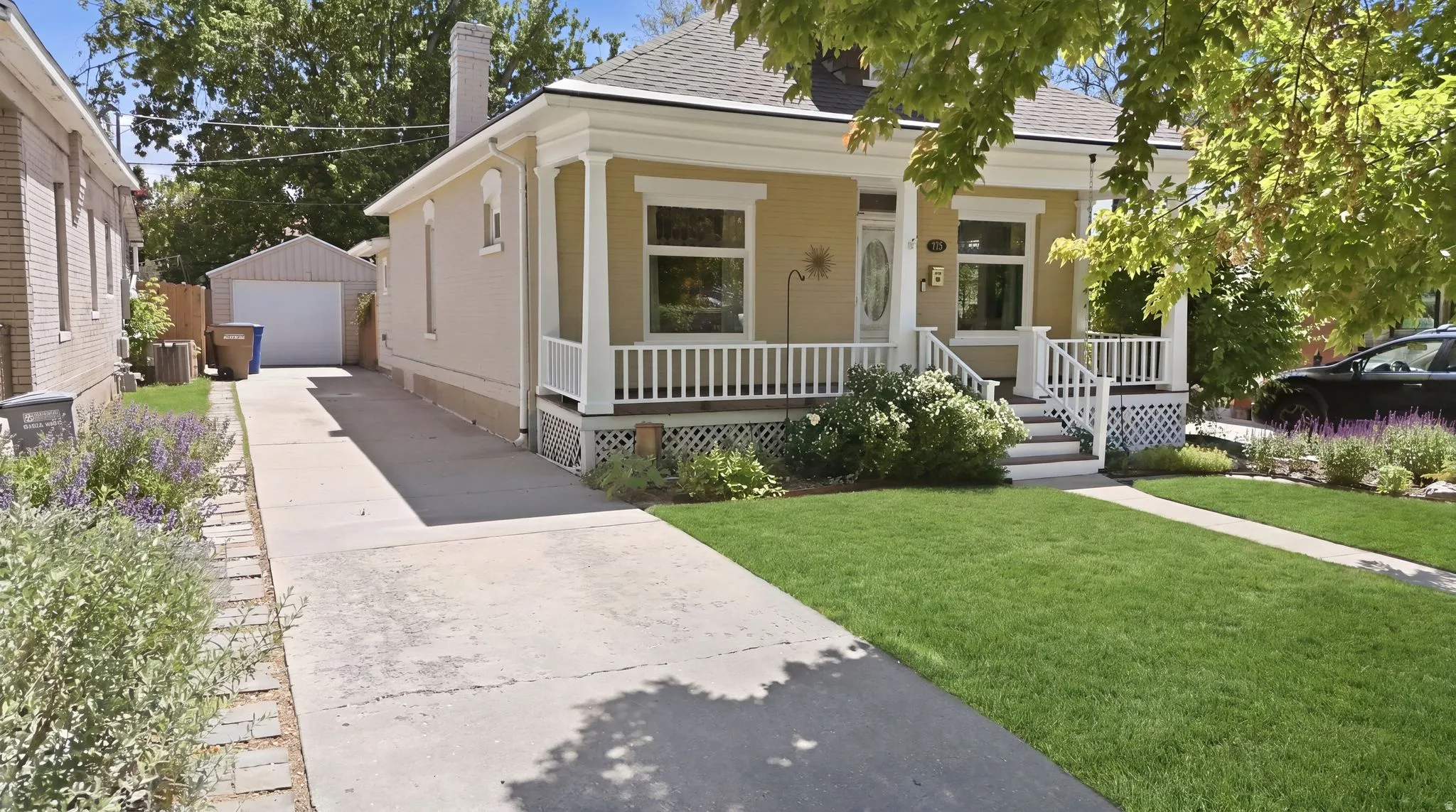 Single-story residence featuring a covered front porch with white railing, a manicured lawn, a detached garage, a concrete driveway, and mature landscaping