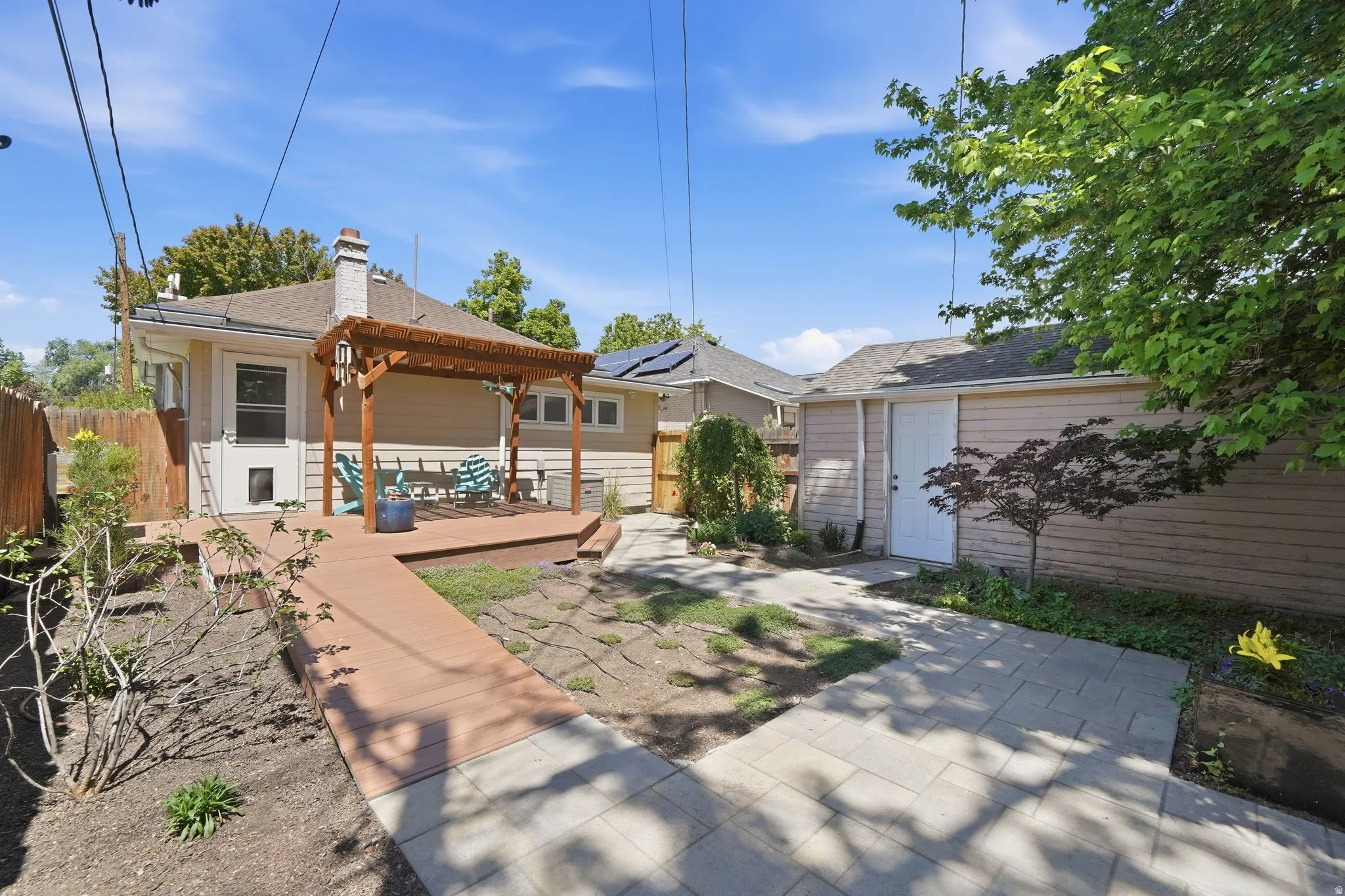 Rear exterior featuring a composite deck with a wood pergola, a paver patio, established landscaping, and a detached structure