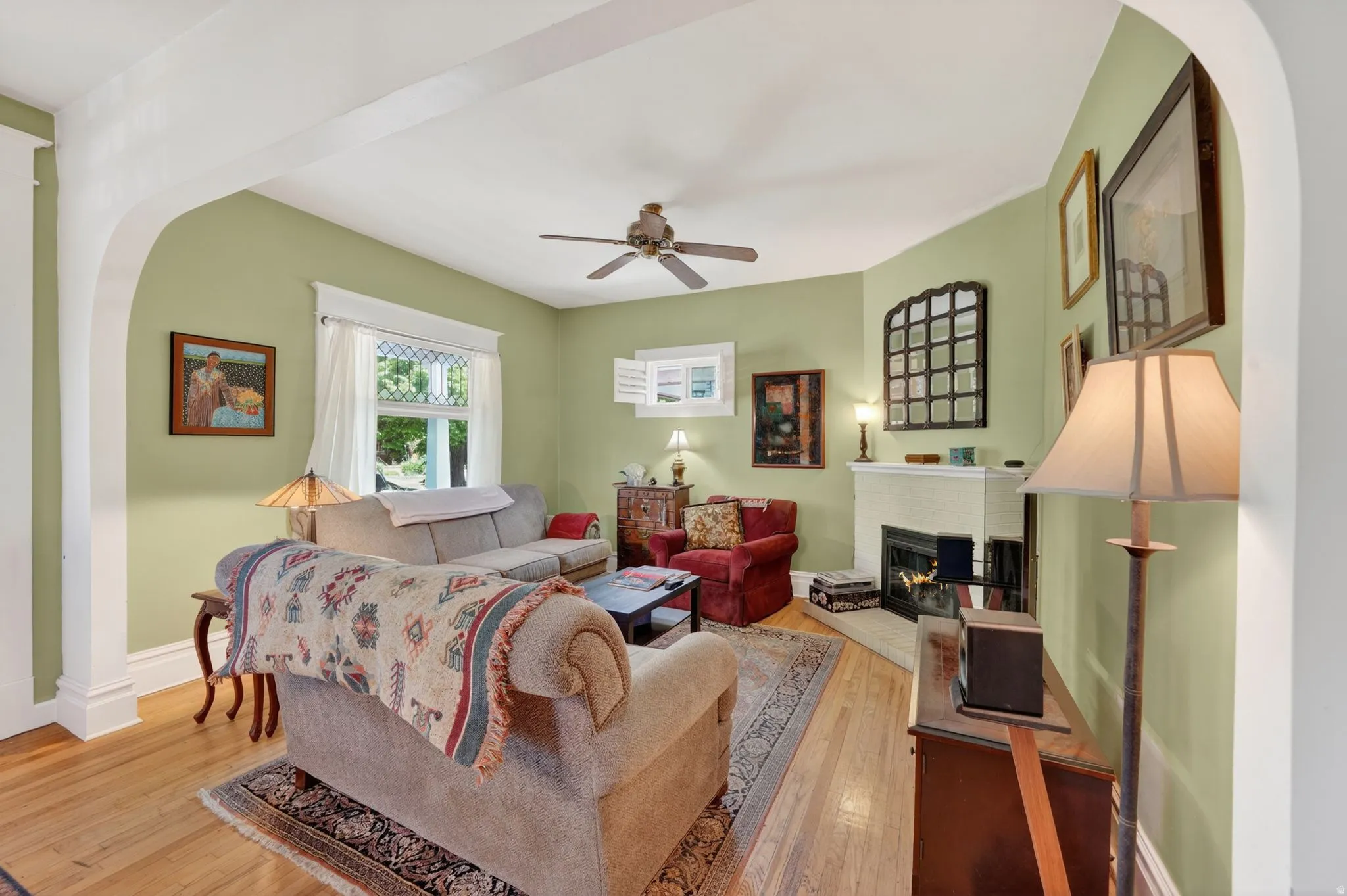 Living space featuring wood-finish flooring, a corner fireplace with a white mantel, and a ceiling fan
