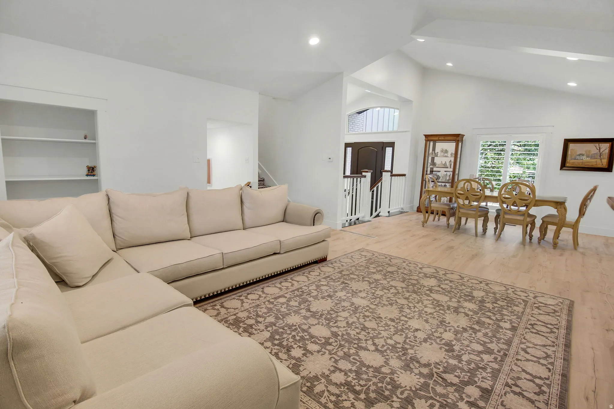 Open-concept living area featuring light wood-finish flooring, vaulted ceilings, recessed lighting, and white plantation shutters