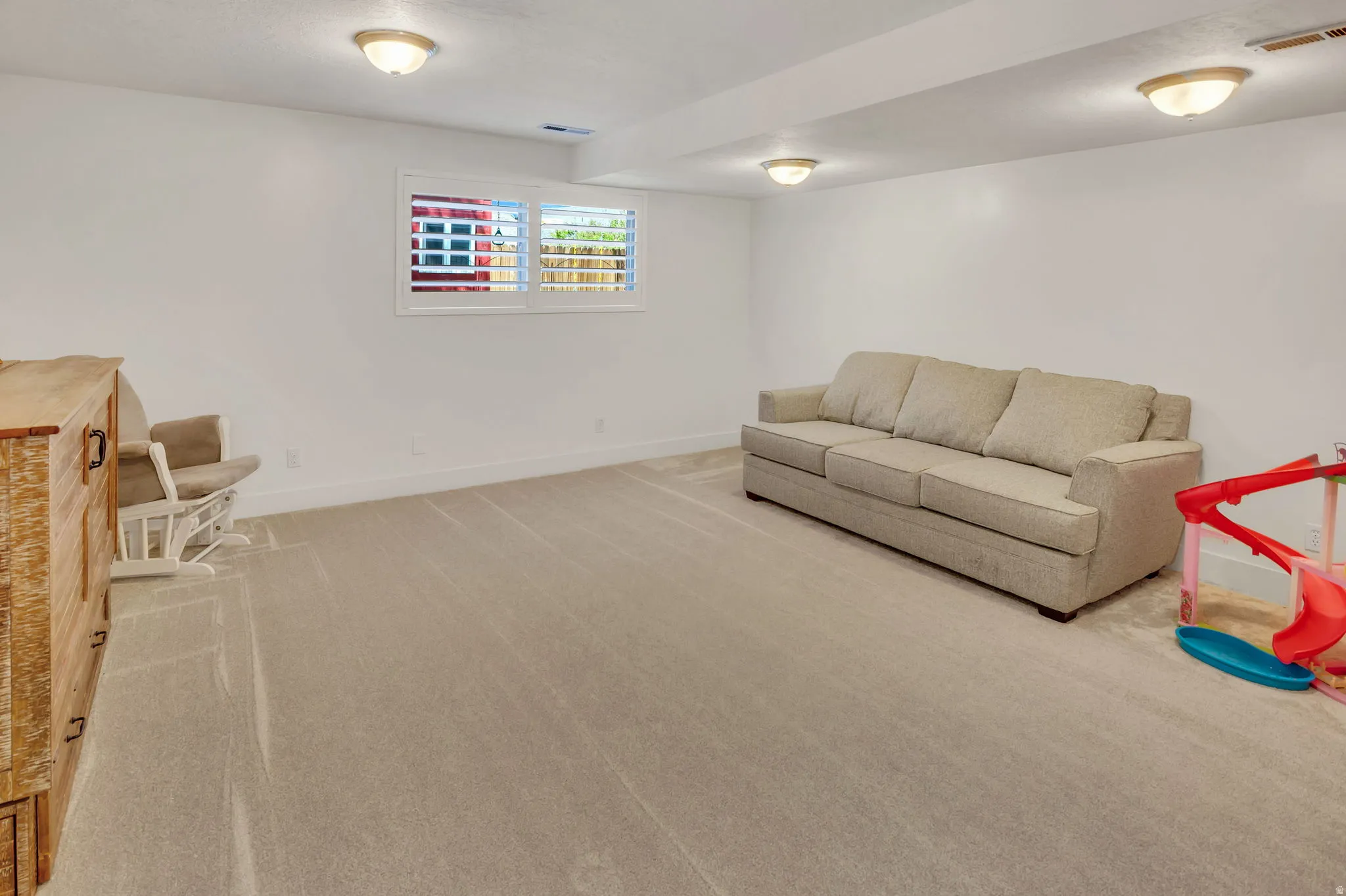 Spacious room featuring neutral carpeting, white walls, and a window with white plantation shutters
