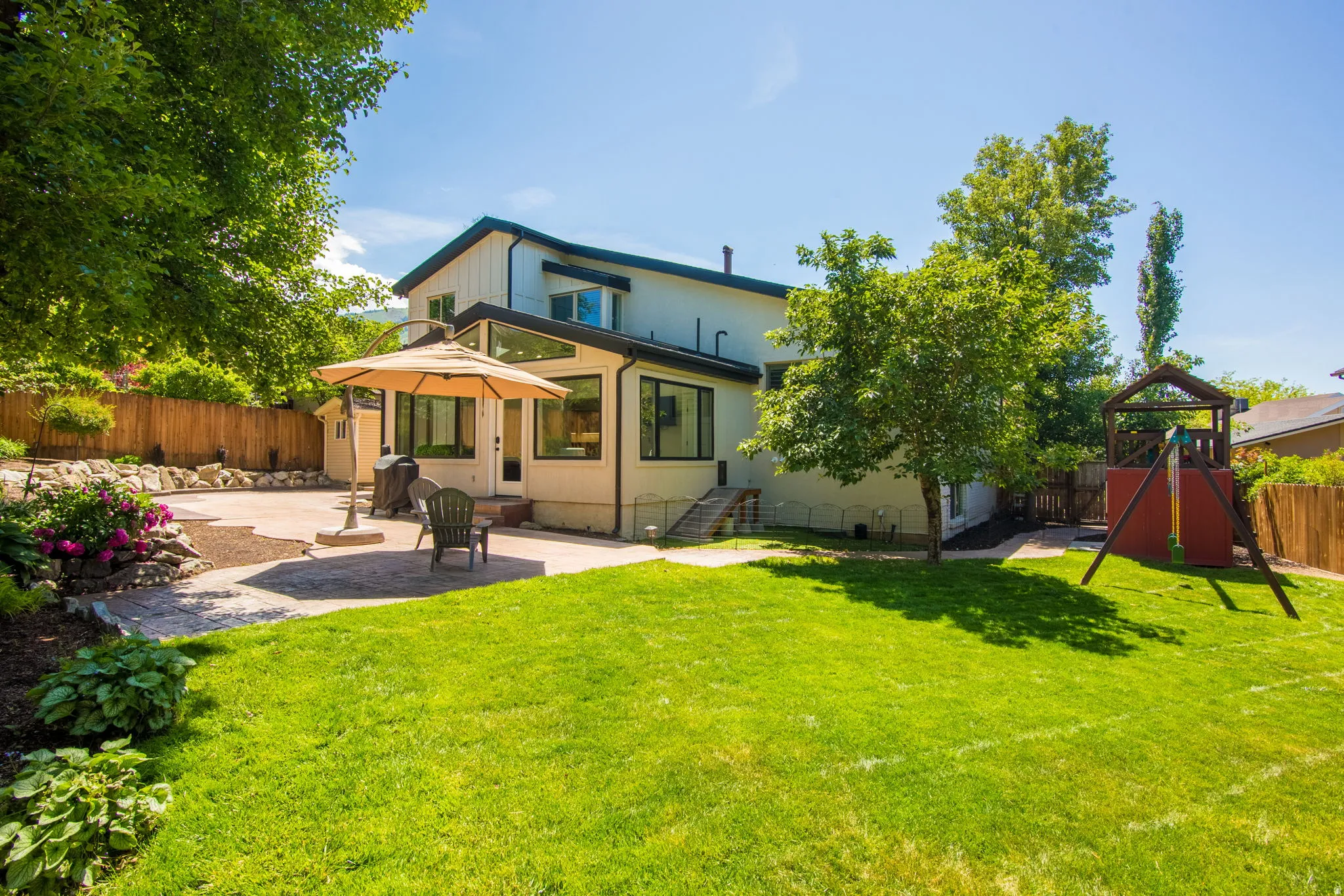 Expansive backyard featuring a lush lawn, a multi-level patio area, mature trees, and a wooden privacy fence