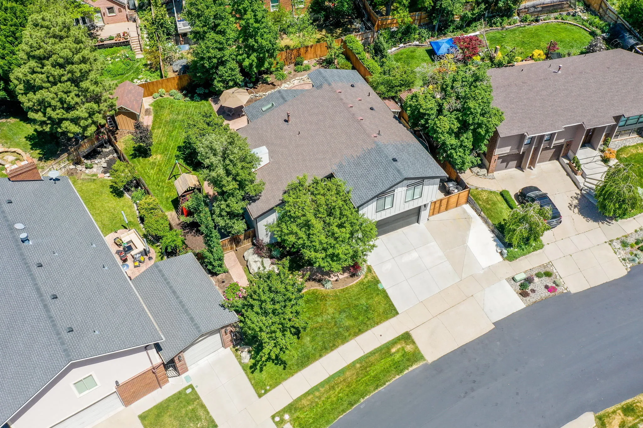 Aerial perspective showcasing the property's exterior, including a concrete driveway, attached garage, and mature trees