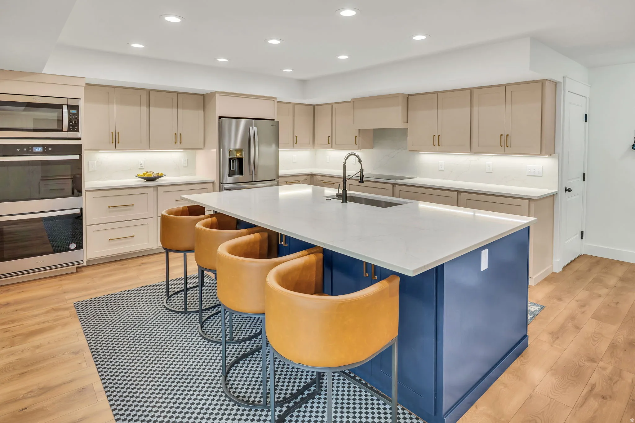 Spacious kitchen featuring a large blue island, light-toned cabinetry, stainless steel appliances, wood-finish flooring, and recessed lighting