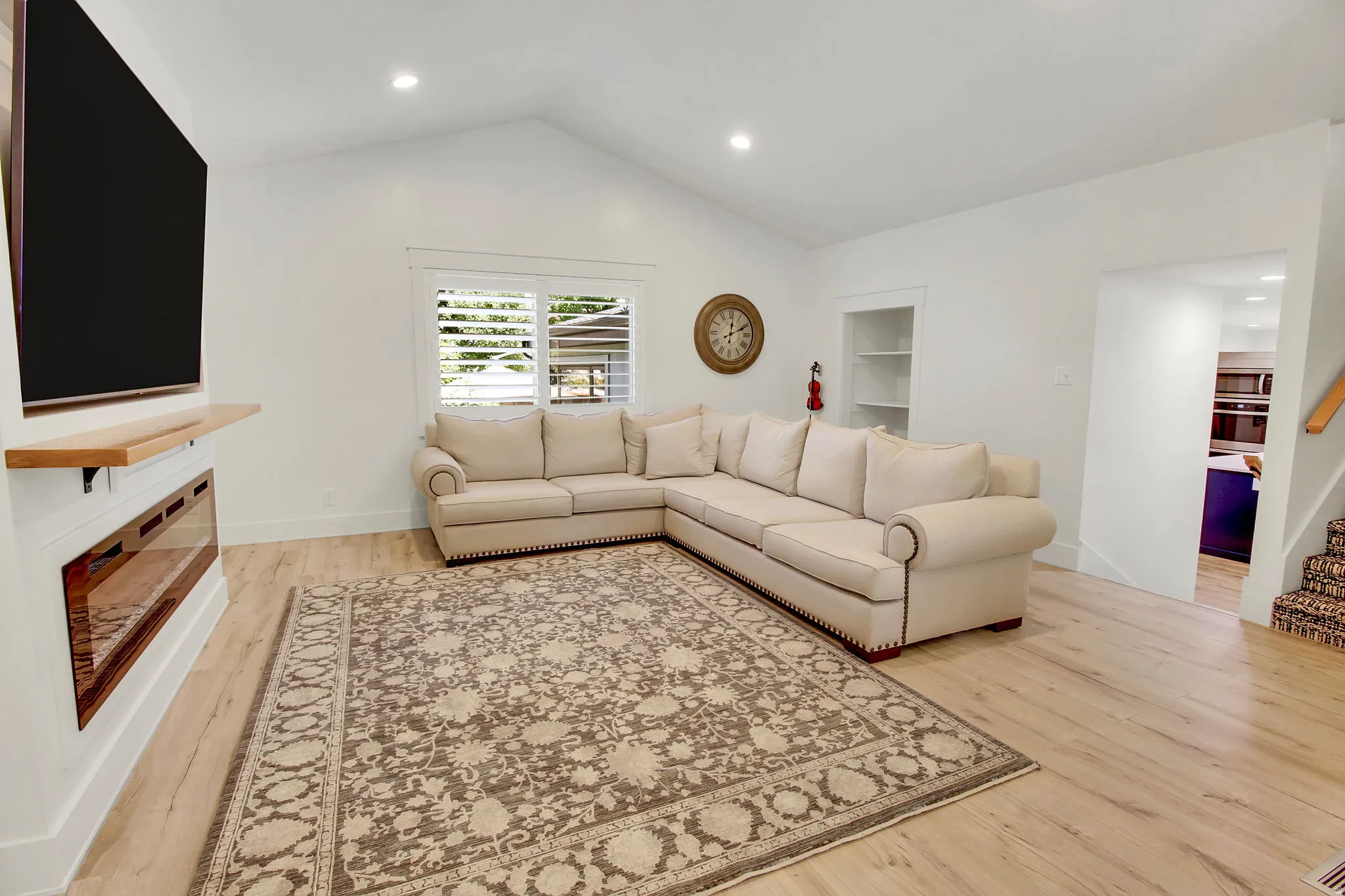 Spacious living area featuring light wood-finish flooring and a vaulted ceiling with recessed lighting