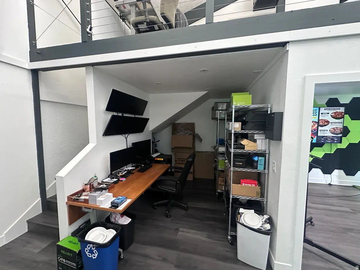 Lower-level workspace featuring wood-finish flooring, a built-in wood desk, and a metal shelving unit