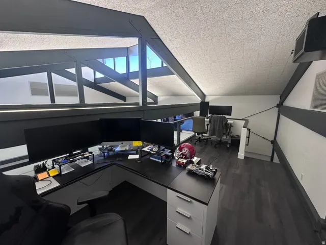 Multifunctional loft space featuring exposed structural beams, high ceilings, dark wood-finish flooring, and natural light from upper windows