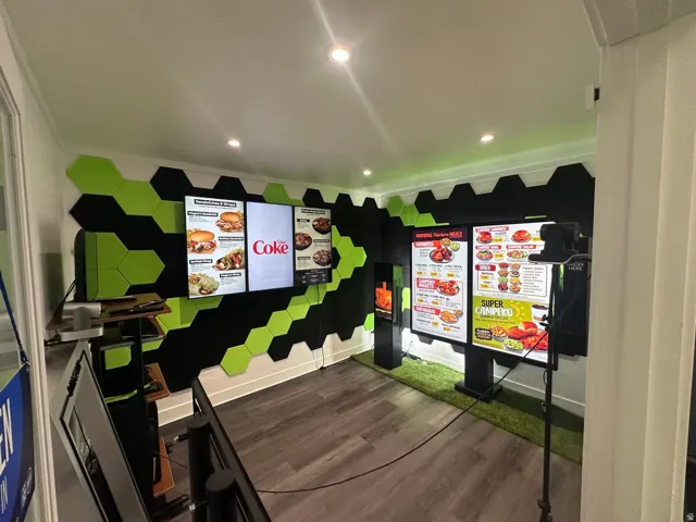 Commercial space featuring multiple digital display menus, hexagonal wall paneling in black and lime green, recessed ceiling lighting, and wood-finish flooring