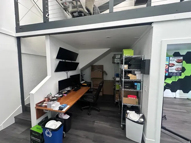 Lower-level workspace featuring wood-finish flooring, a built-in wood desk, and a metal shelving unit