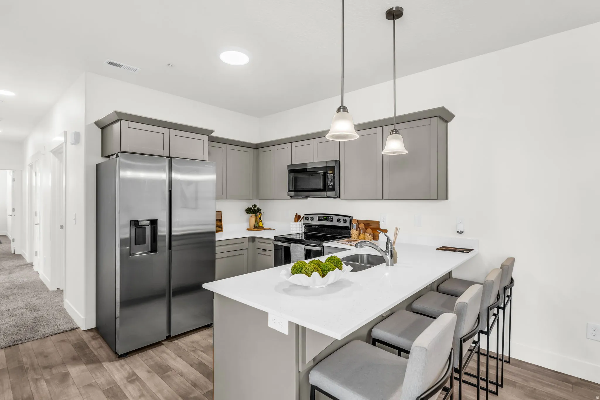 Modern kitchen featuring wood-finish flooring, gray cabinetry, stainless steel appliances, white countertops, and pendant lighting