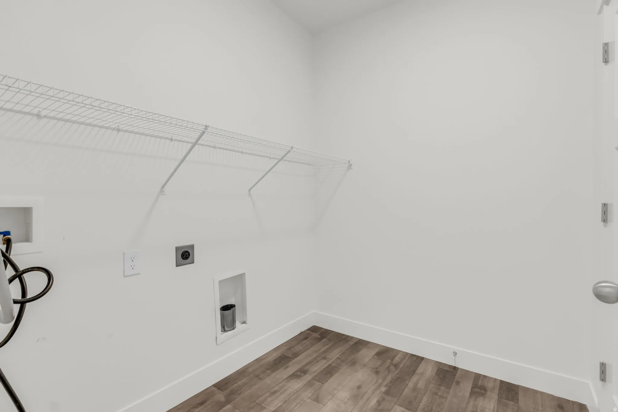 Dedicated laundry area featuring white wire shelving, a wood-finish floor, and bright white walls