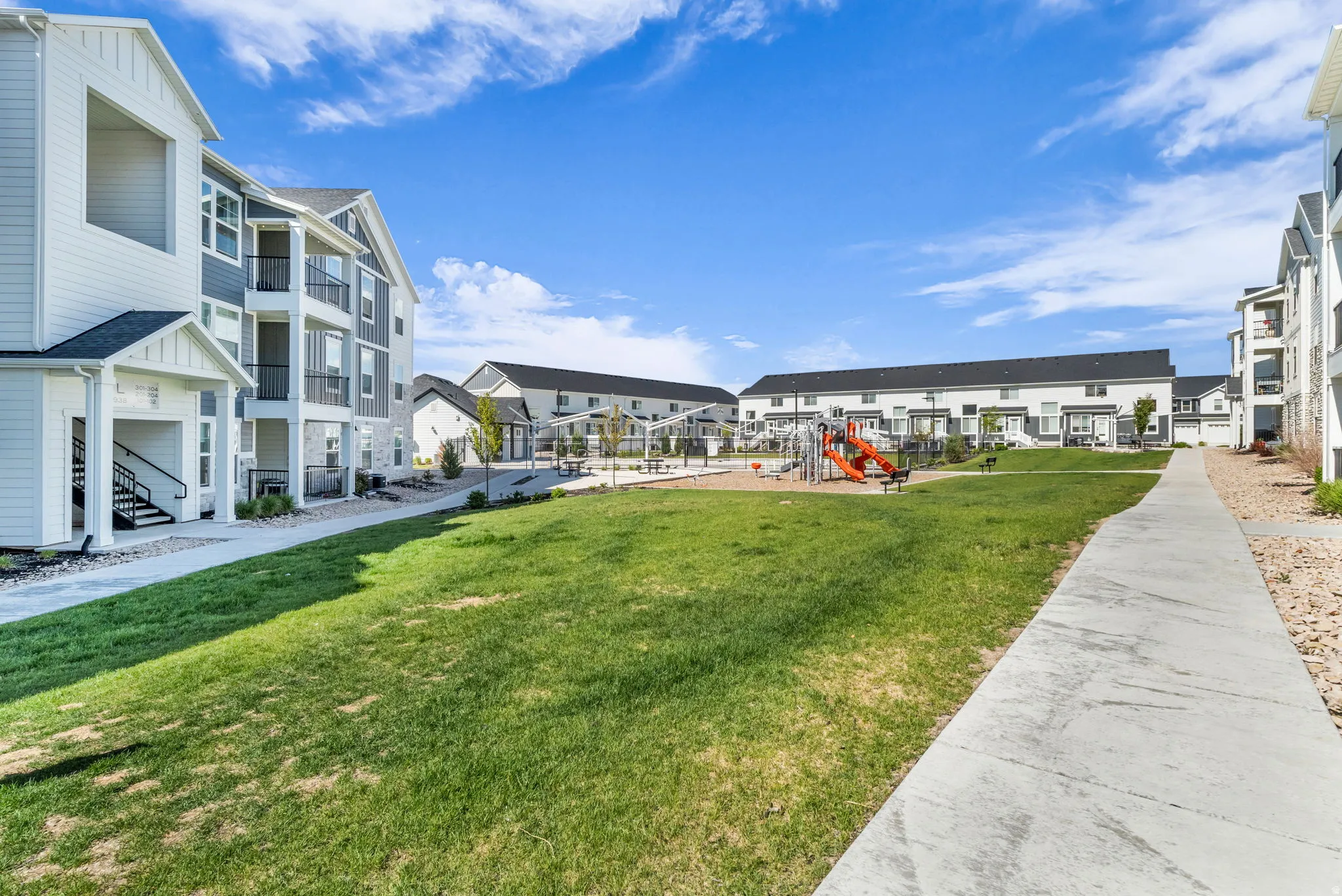 Expansive green space featuring a playground with a slide and swings, surrounded by modern residential buildings