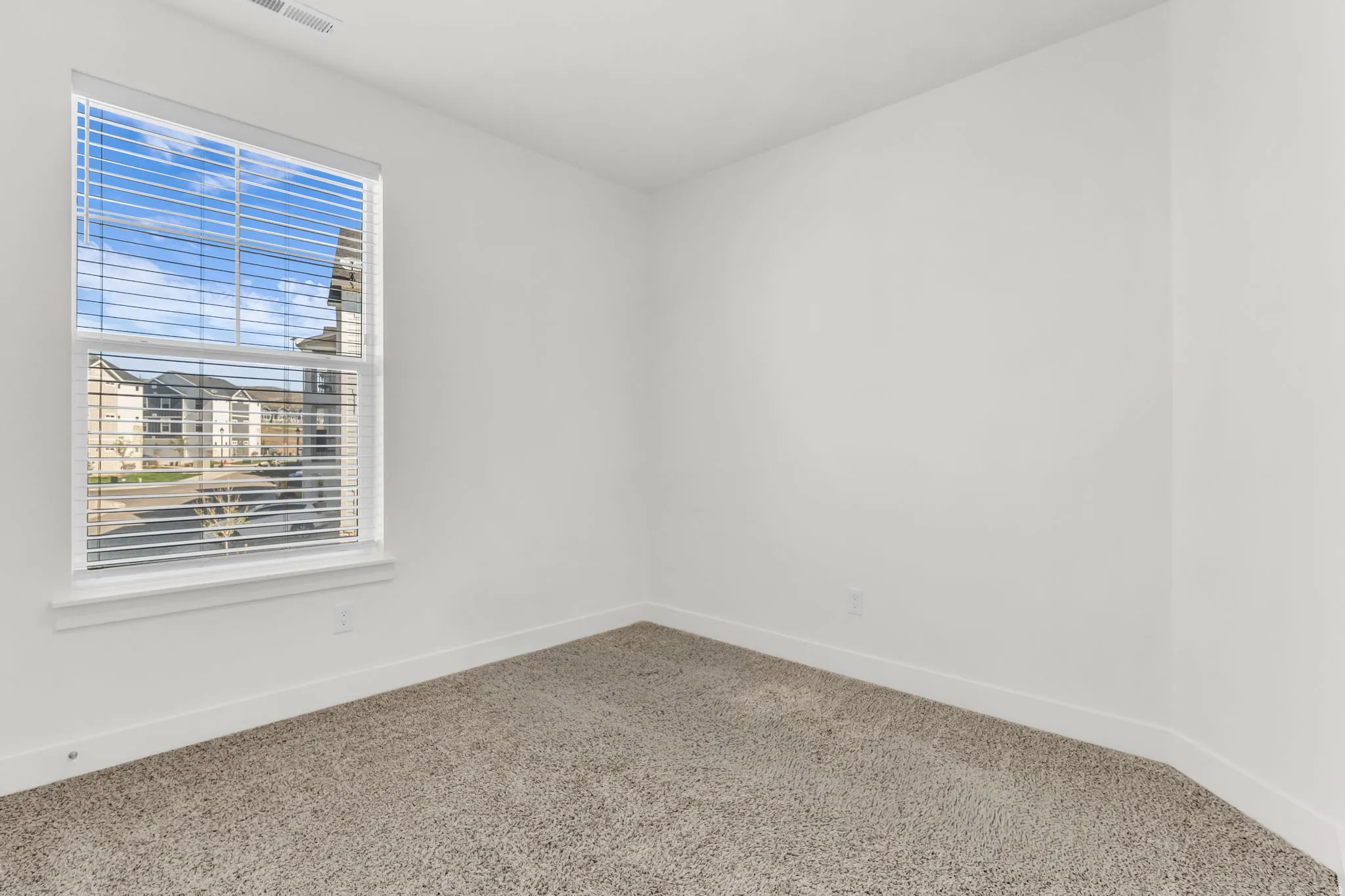 Bright interior space featuring a window with integrated blinds, clean white walls, and neutral-toned carpeting