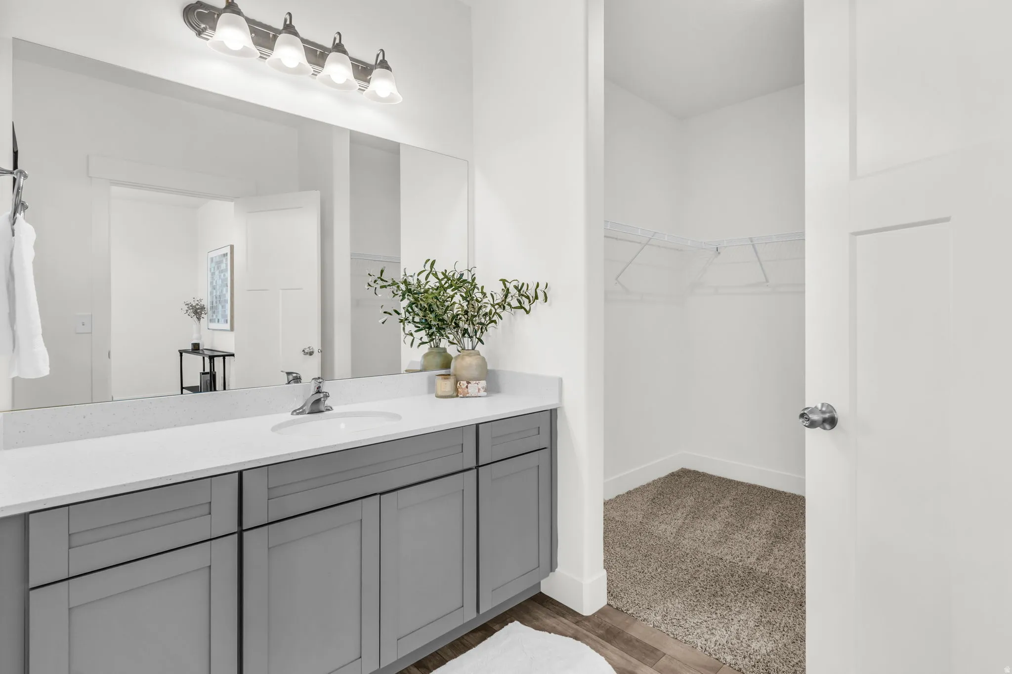 Bathroom featuring a light-toned countertop, an integrated single sink, a wide vanity mirror, and a vanity with gray cabinetry