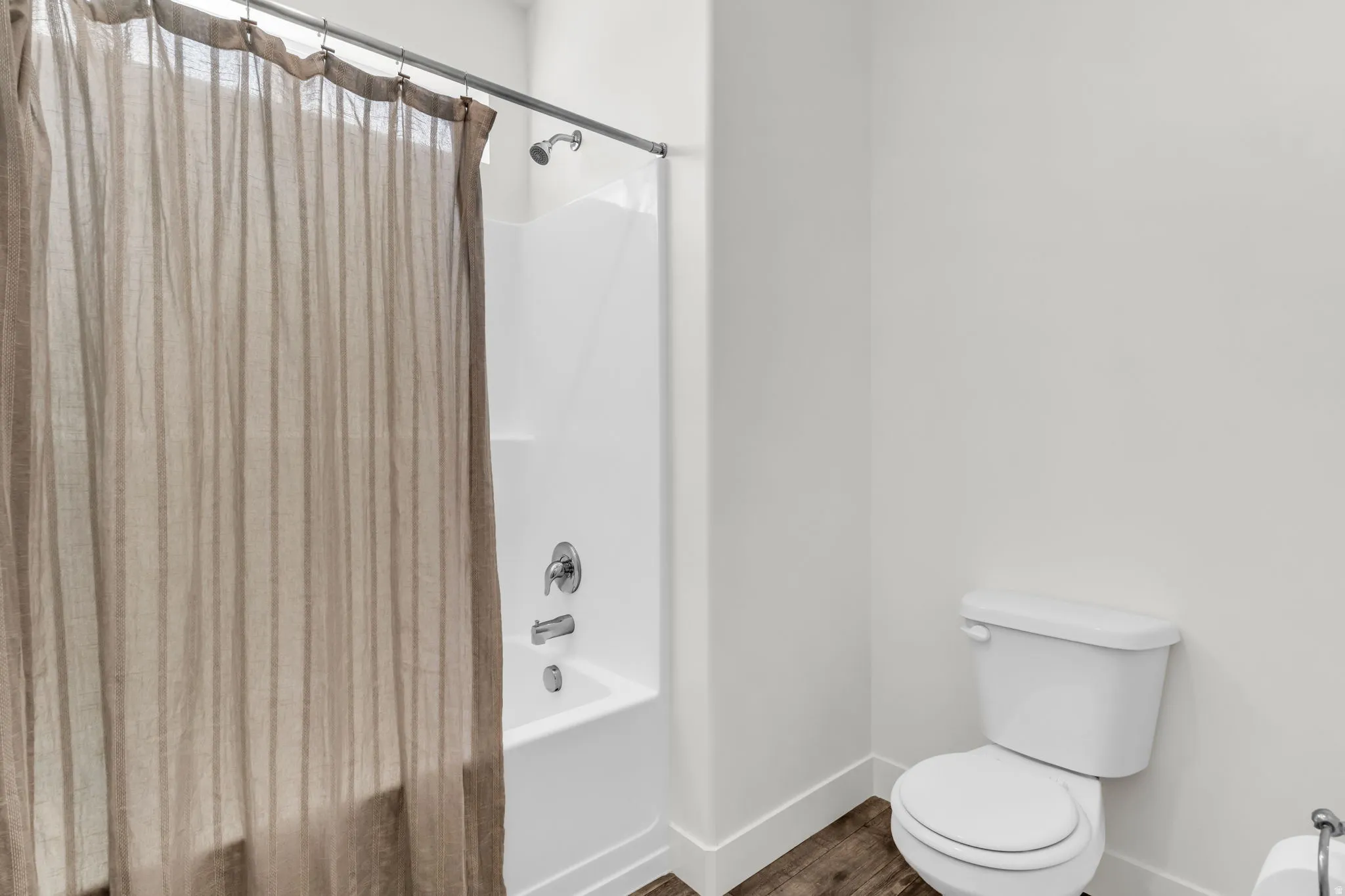 Bathroom featuring a white tub/shower combination with chrome fixtures, a white toilet, and wood-finish flooring
