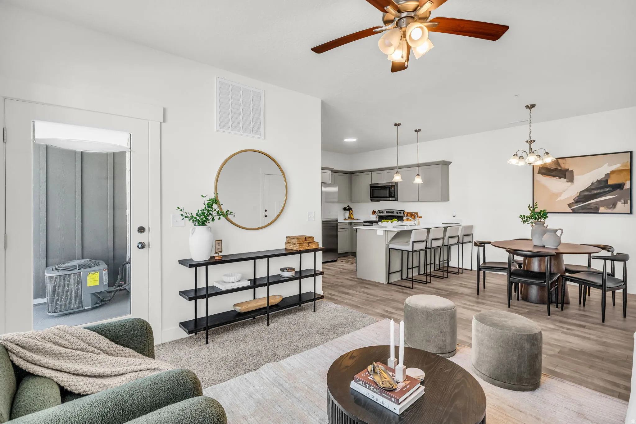 Open-concept living space featuring wood-finish flooring, a contemporary kitchen with grey cabinetry and an island, a dining area with a chandelier, and a ceiling fan in the living room