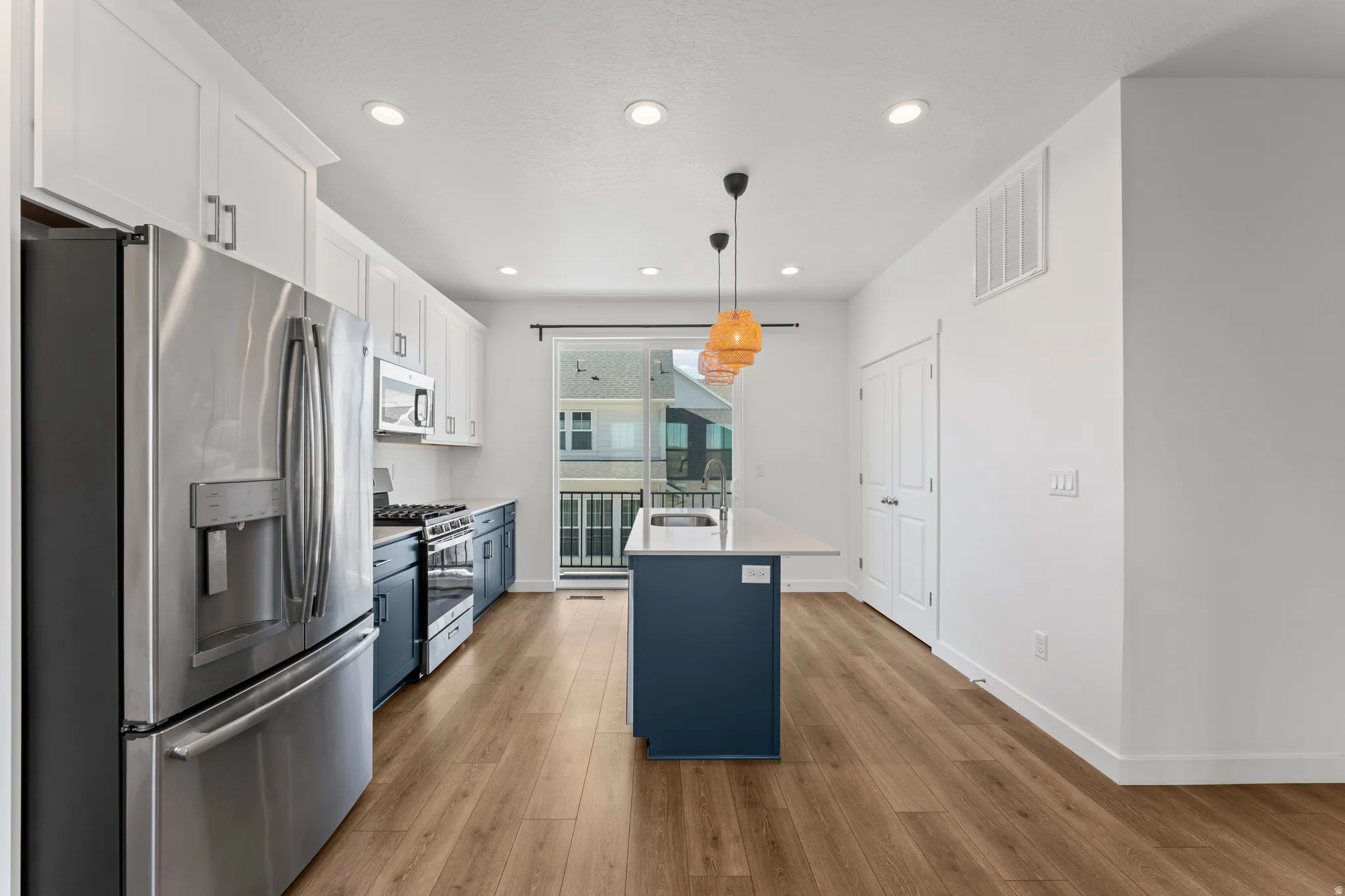Open-concept kitchen featuring wood-finish flooring, white upper cabinetry, deep blue lower cabinetry, stainless steel appliances, and a central island with a light-colored countertop